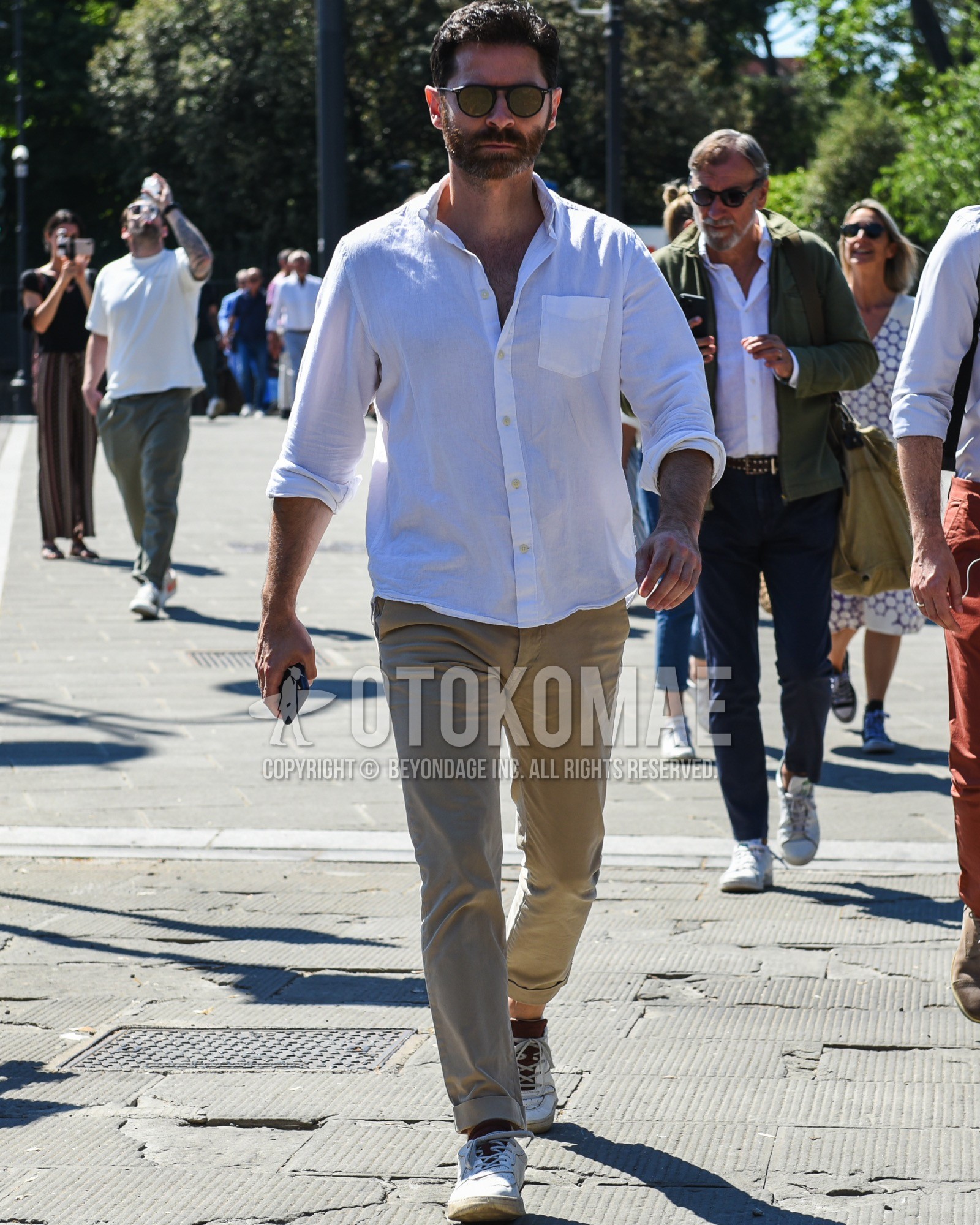 Men's spring summer outfit with black plain sunglasses, white plain shirt, beige plain chinos, white low-cut sneakers.