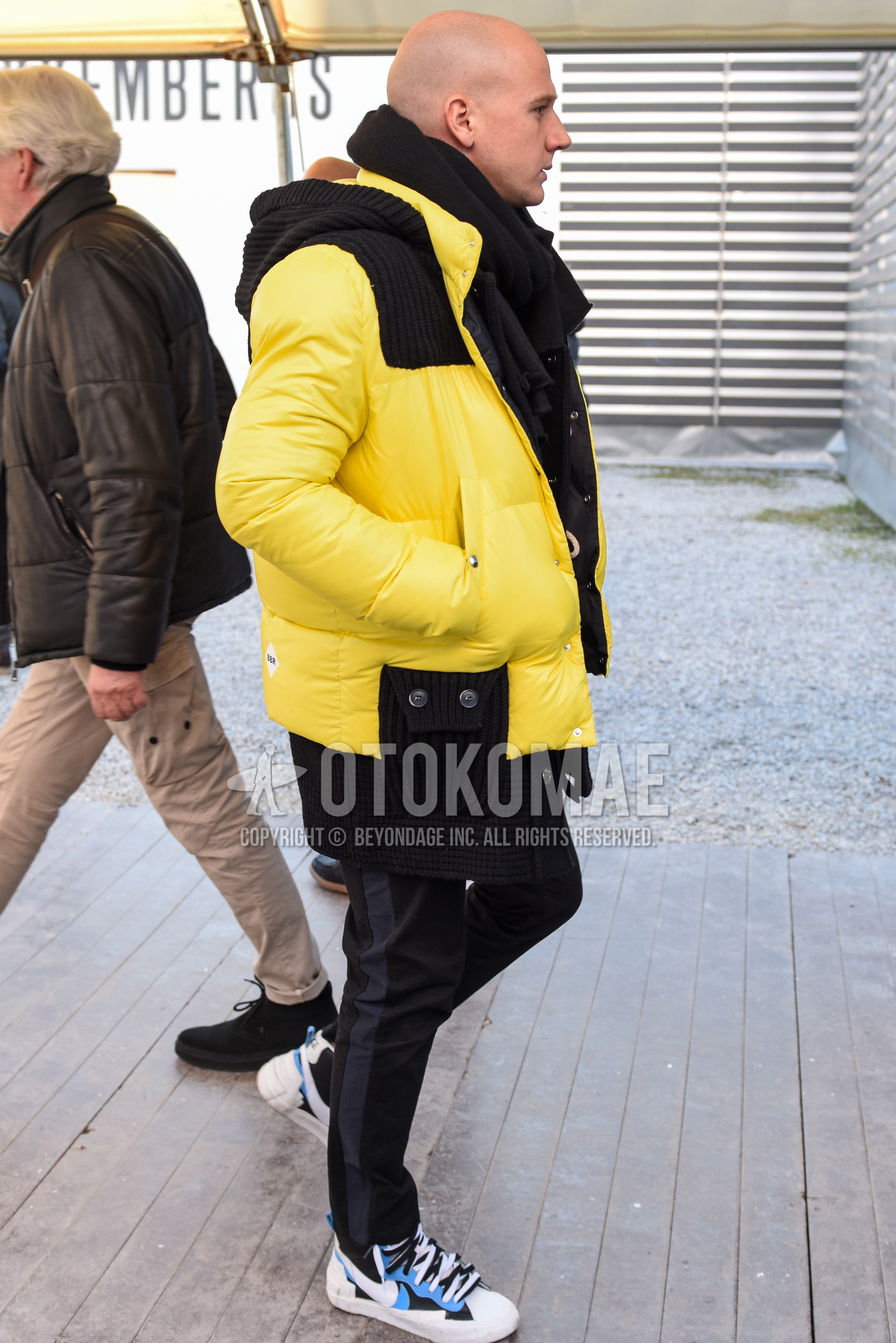 Men's winter outfit with black plain scarf, yellow black plain down jacket, black plain sideline pants, light blue white high-cut sneakers.
