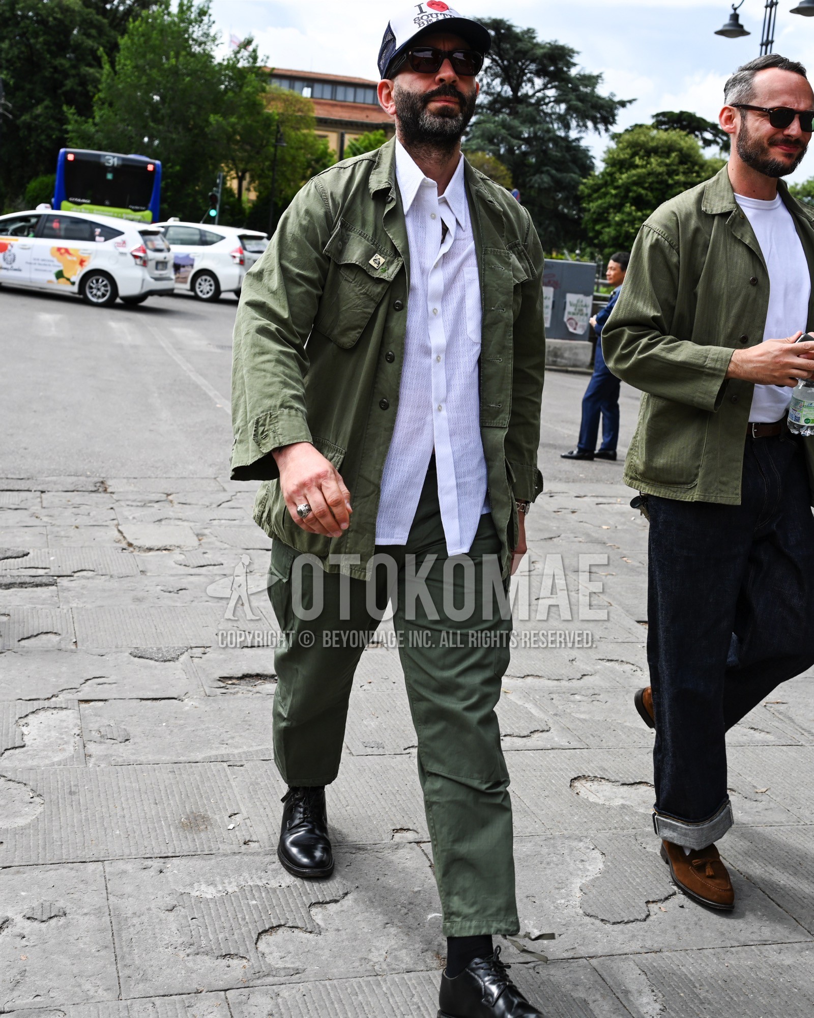 Men's spring summer autumn outfit with black deca logo baseball cap, olive green plain military jacket, white plain shirt, olive green plain chinos, black plain toe leather shoes.
