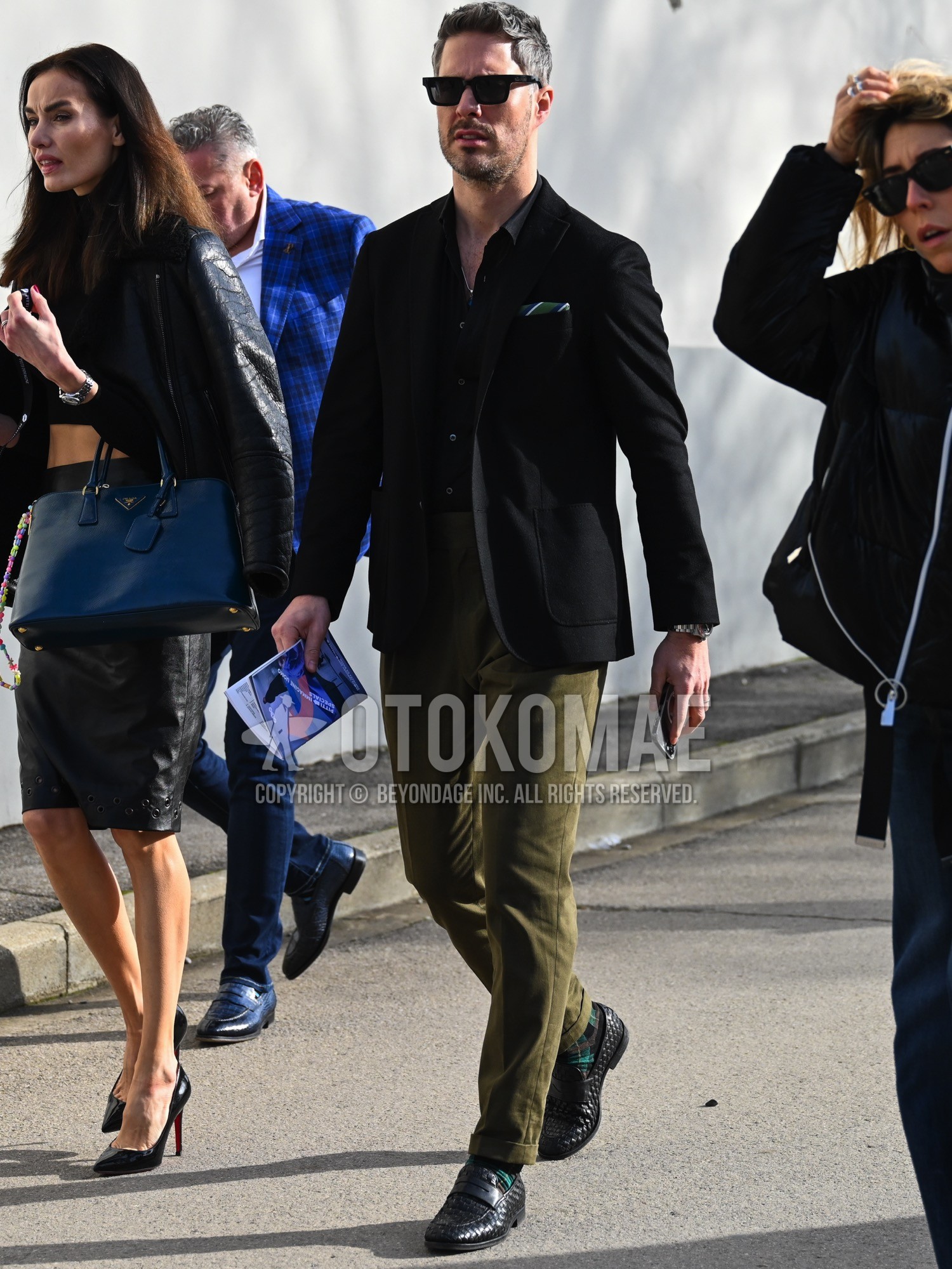 Men's autumn winter outfit with black plain sunglasses, black plain tailored jacket, black plain shirt, olive green plain slacks, green check socks, black coin loafers leather shoes.