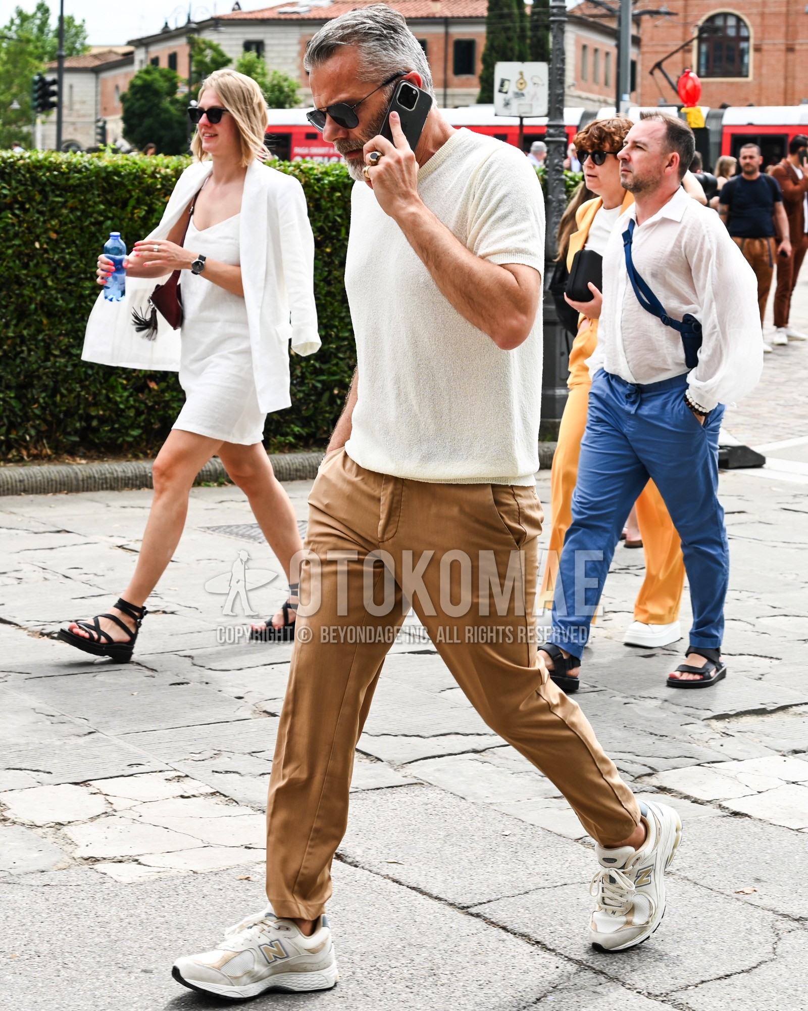 Men's spring summer outfit with black plain sunglasses, white plain t-shirt, brown plain chinos, white low-cut sneakers.