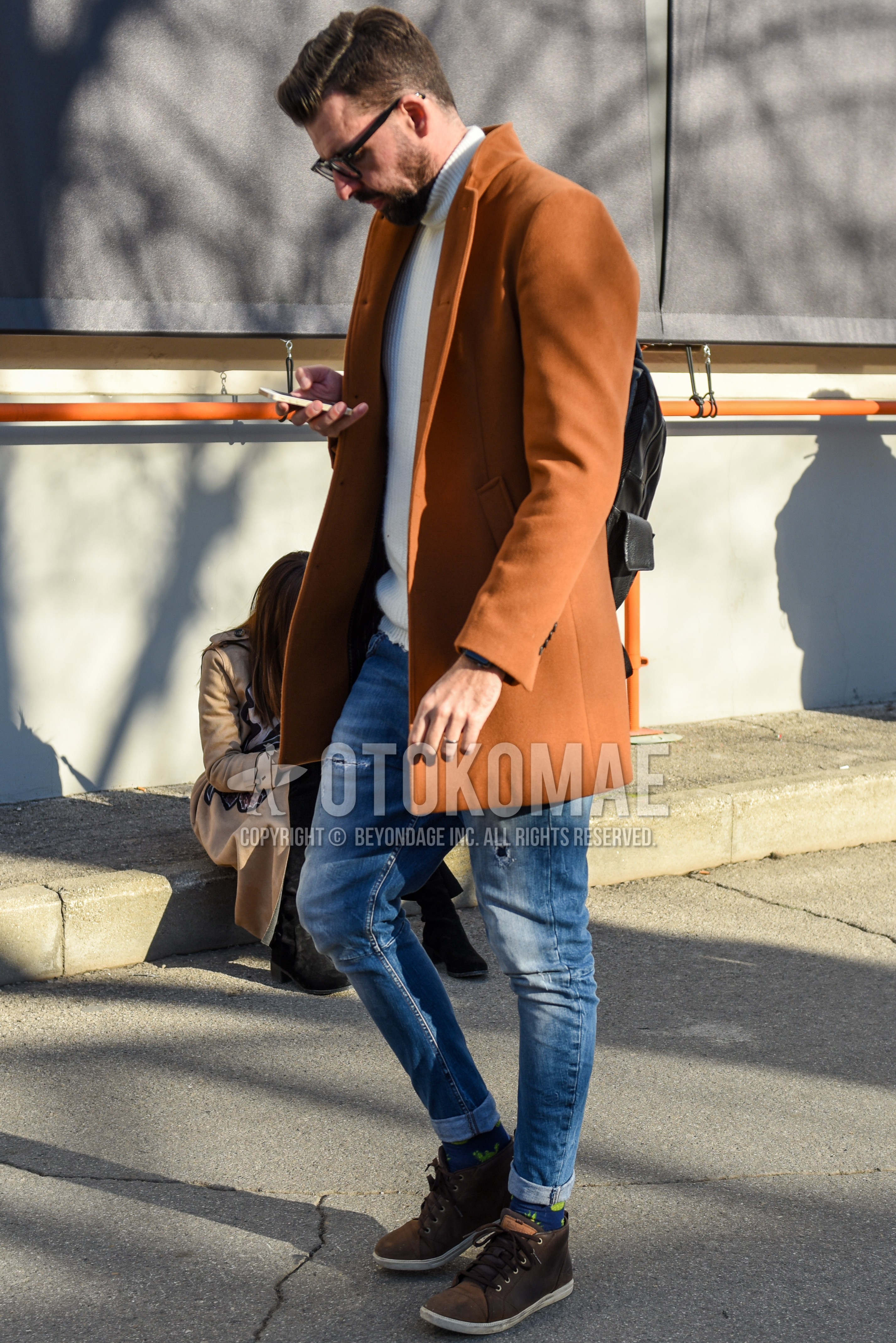 Men's autumn winter outfit with black plain glasses, brown plain chester coat, white plain turtleneck knit, blue plain damaged jeans, blue socks socks, brown high-cut sneakers, black plain backpack.