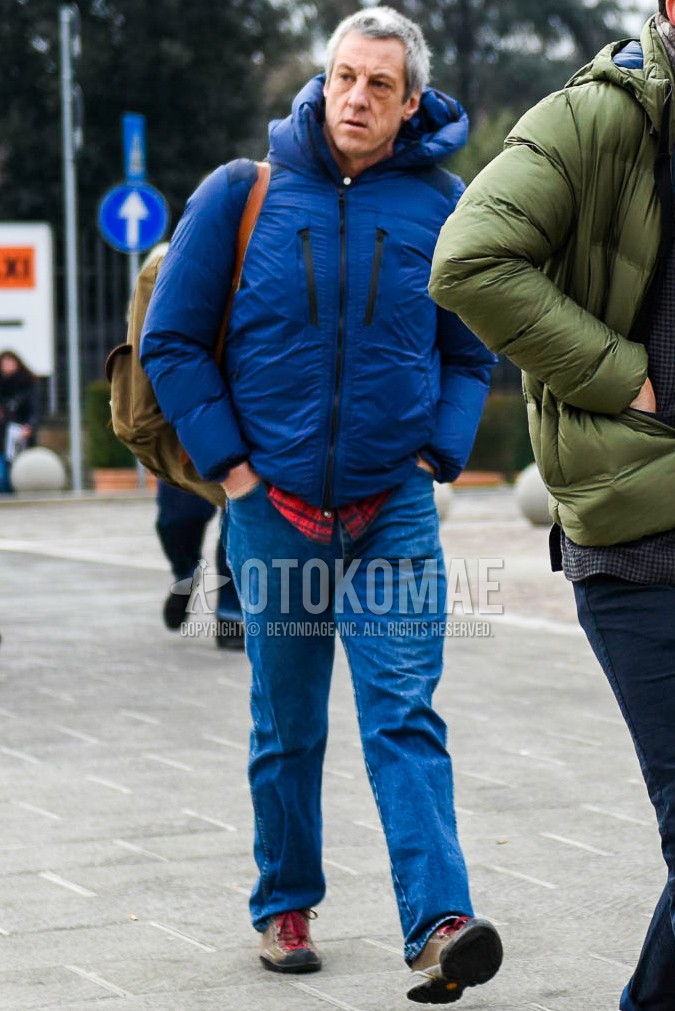 Men's winter outfit with blue plain down jacket, red check shirt, blue plain denim/jeans, beige low-cut sneakers.