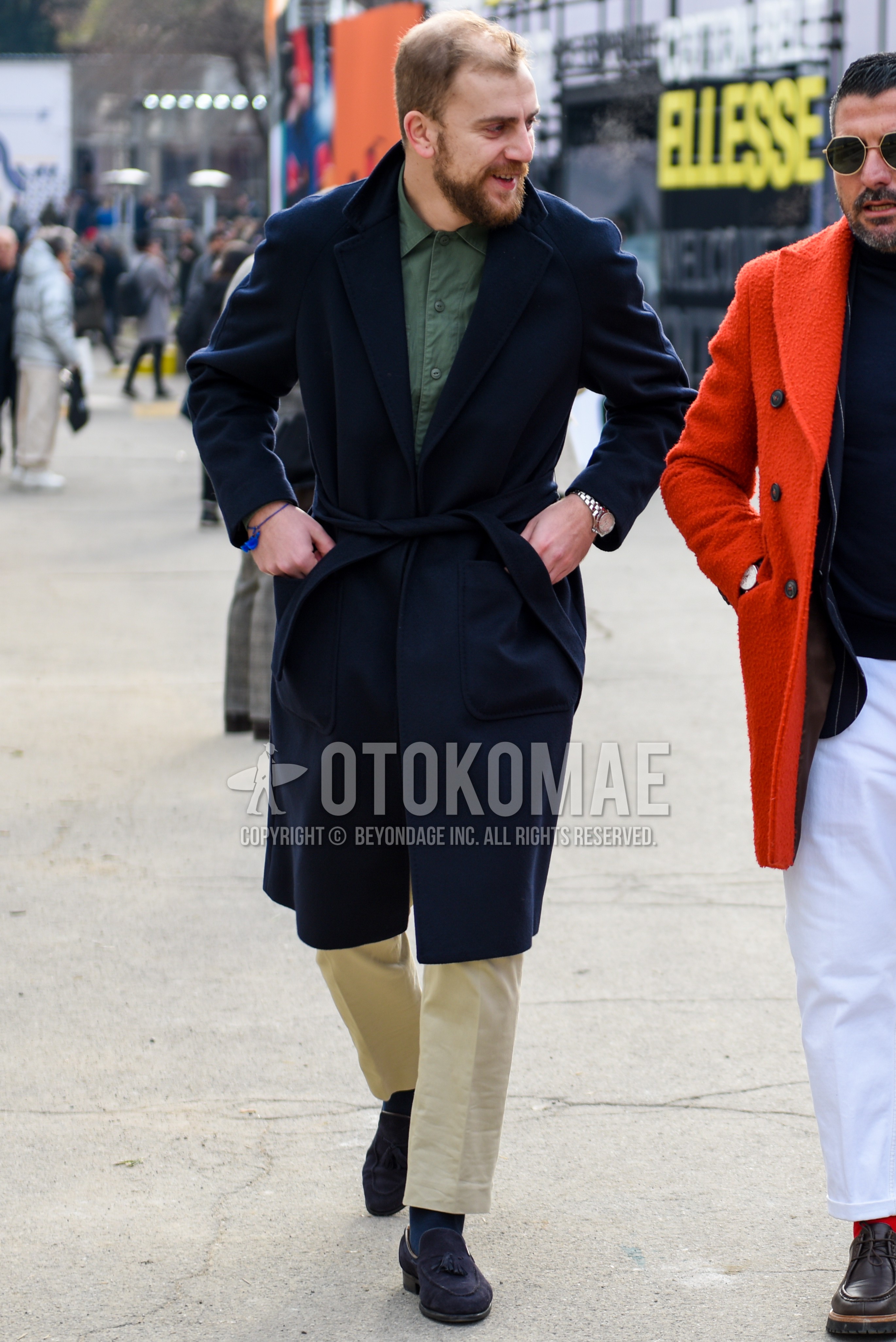 Men's autumn winter outfit with navy plain belted coat, green plain shirt, beige plain chinos, beige plain ankle pants, navy plain socks, navy tassel loafers leather shoes.