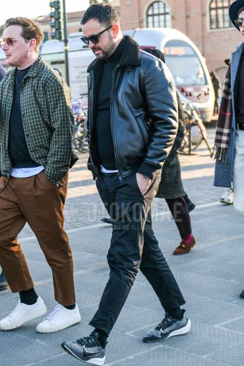 黒無地のサングラス、黒無地のレザージャケット(ライダース以外)、黒無地のミリタリージャケット(MA-1、M-65以外)、ダークグレー無地のタートルネックニット、黒無地のコットンパンツ、黒無地のアンクルパンツ、黒無地のソックス、ナイキのグレーローカットのスニーカーを合わせた秋冬のメンズコーデ・着こなし。