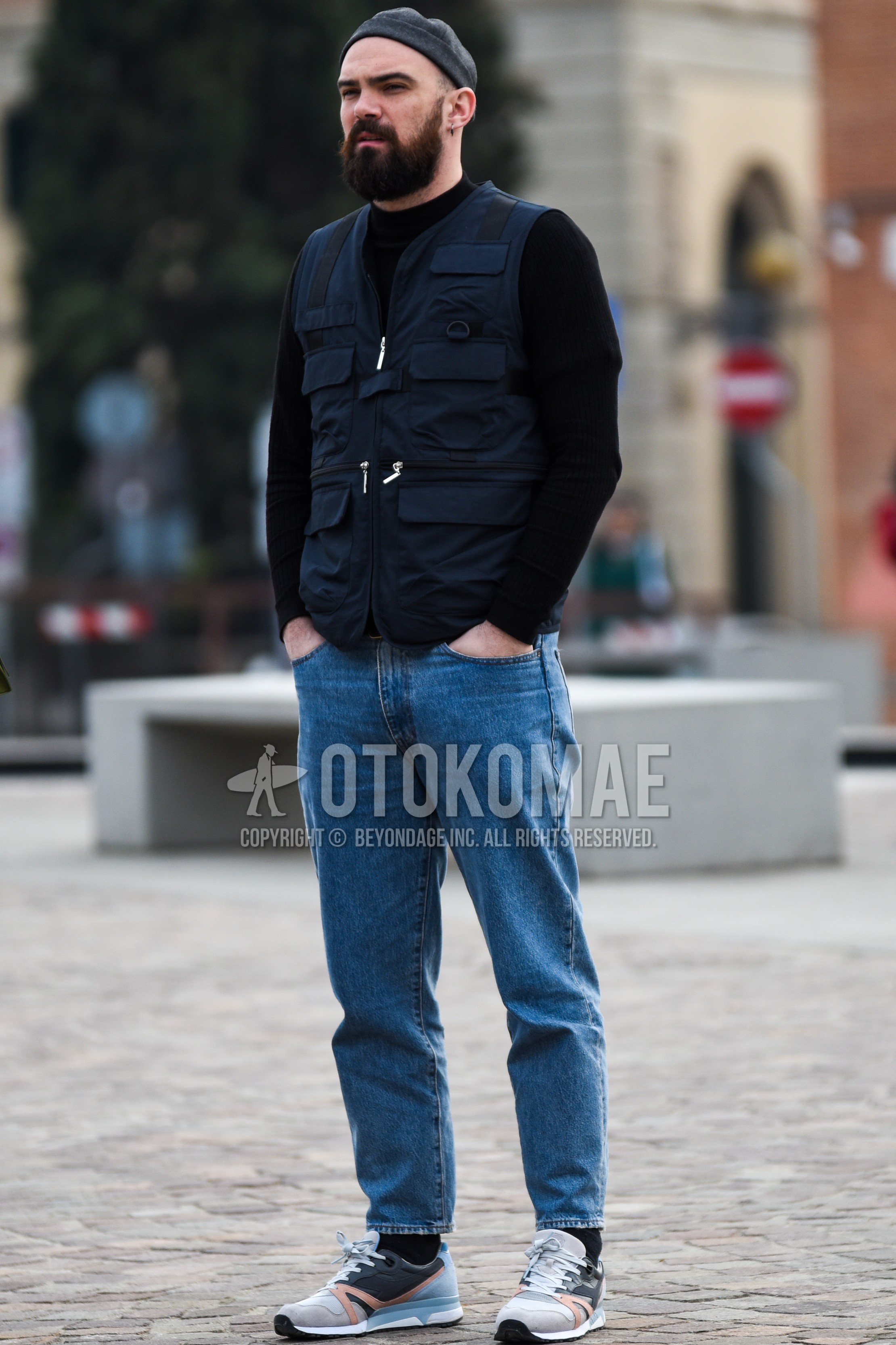 Men's spring autumn outfit with gray plain cap, navy plain casual vest, black plain sweater, blue plain denim/jeans, black plain socks, gray low-cut sneakers.