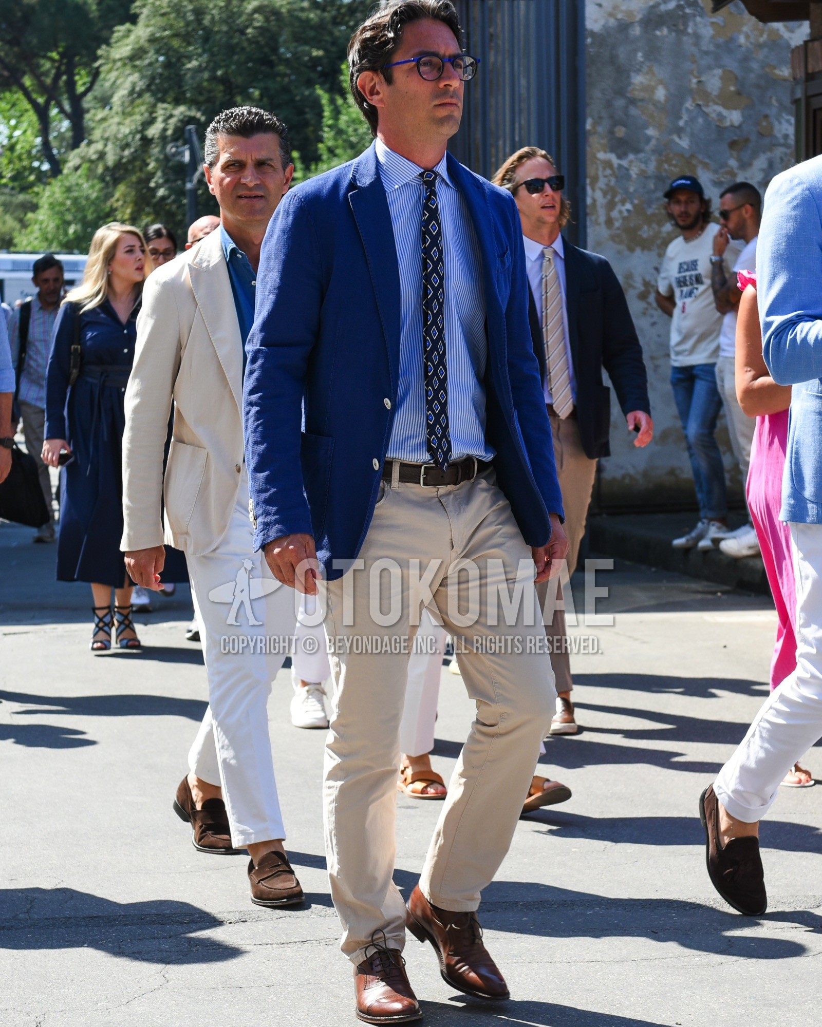Men's spring summer outfit with blue plain glasses, blue plain tailored jacket, blue white stripes shirt, brown plain leather belt, beige plain chinos, navy small crest necktie.