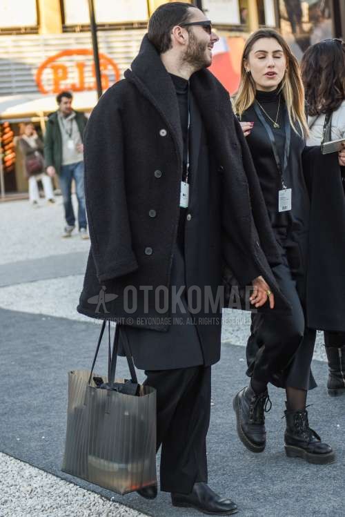 黒無地のサングラス、黒無地のアウター、ダークグレー無地のアウター、黒無地のTシャツ、黒無地のスラックス、黒のブーツ、クリア無地のブリーフケース/ハンドバッグを合わせた冬秋のメンズコーデ・着こなし。