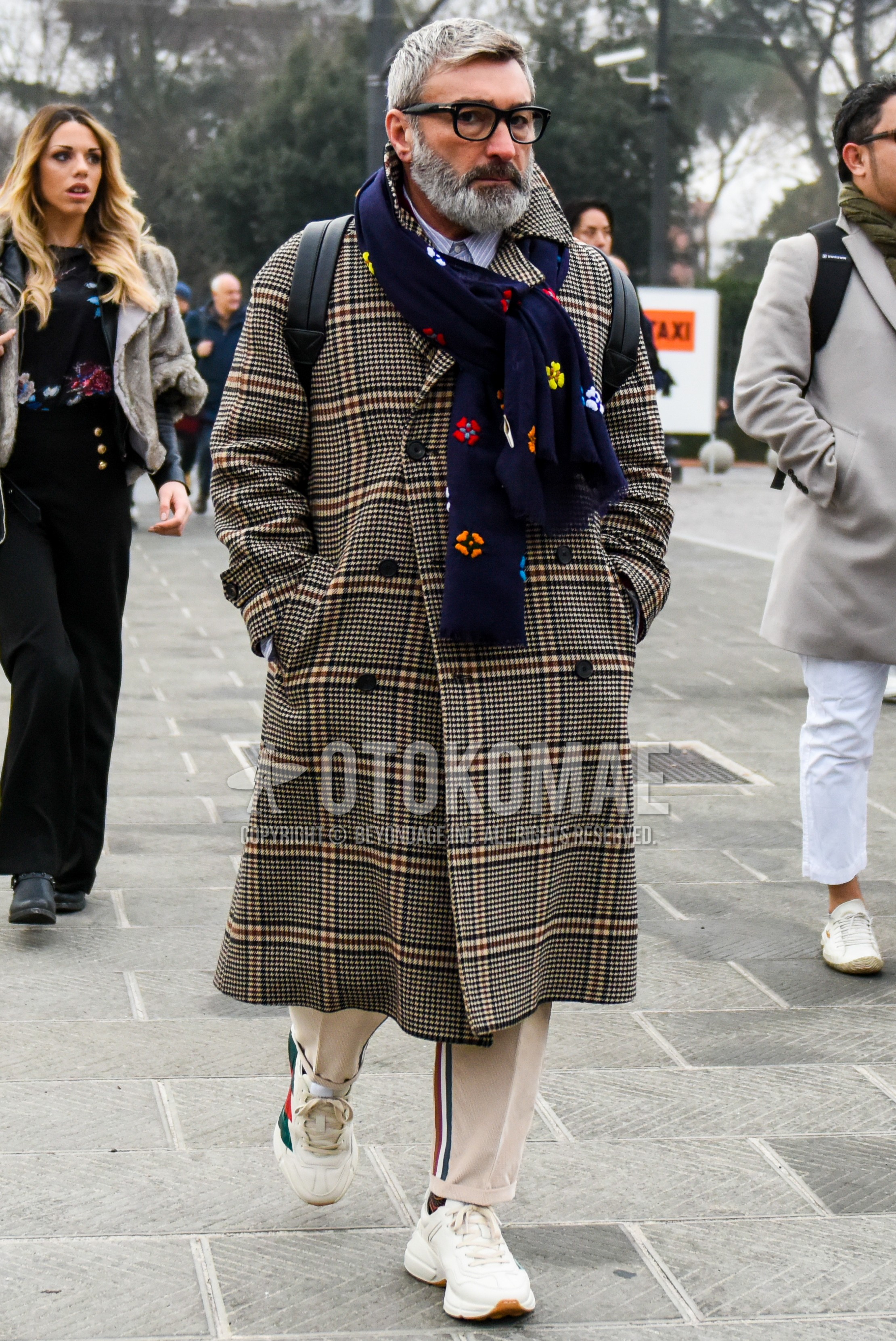 Men's autumn winter outfit with plain glasses, navy scarf scarf, beige check chester coat, beige plain sideline pants, white low-cut sneakers.