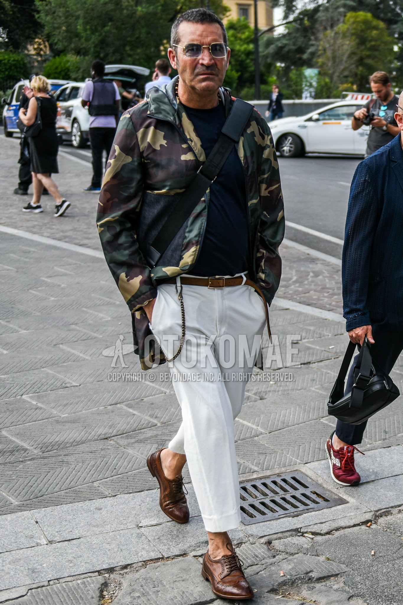 Men's spring autumn outfit with silver plain sunglasses, olive green camouflage hooded coat, navy plain t-shirt, brown plain leather belt, white plain pleated pants, plain cotton pants, brown wing-tip shoes leather shoes.