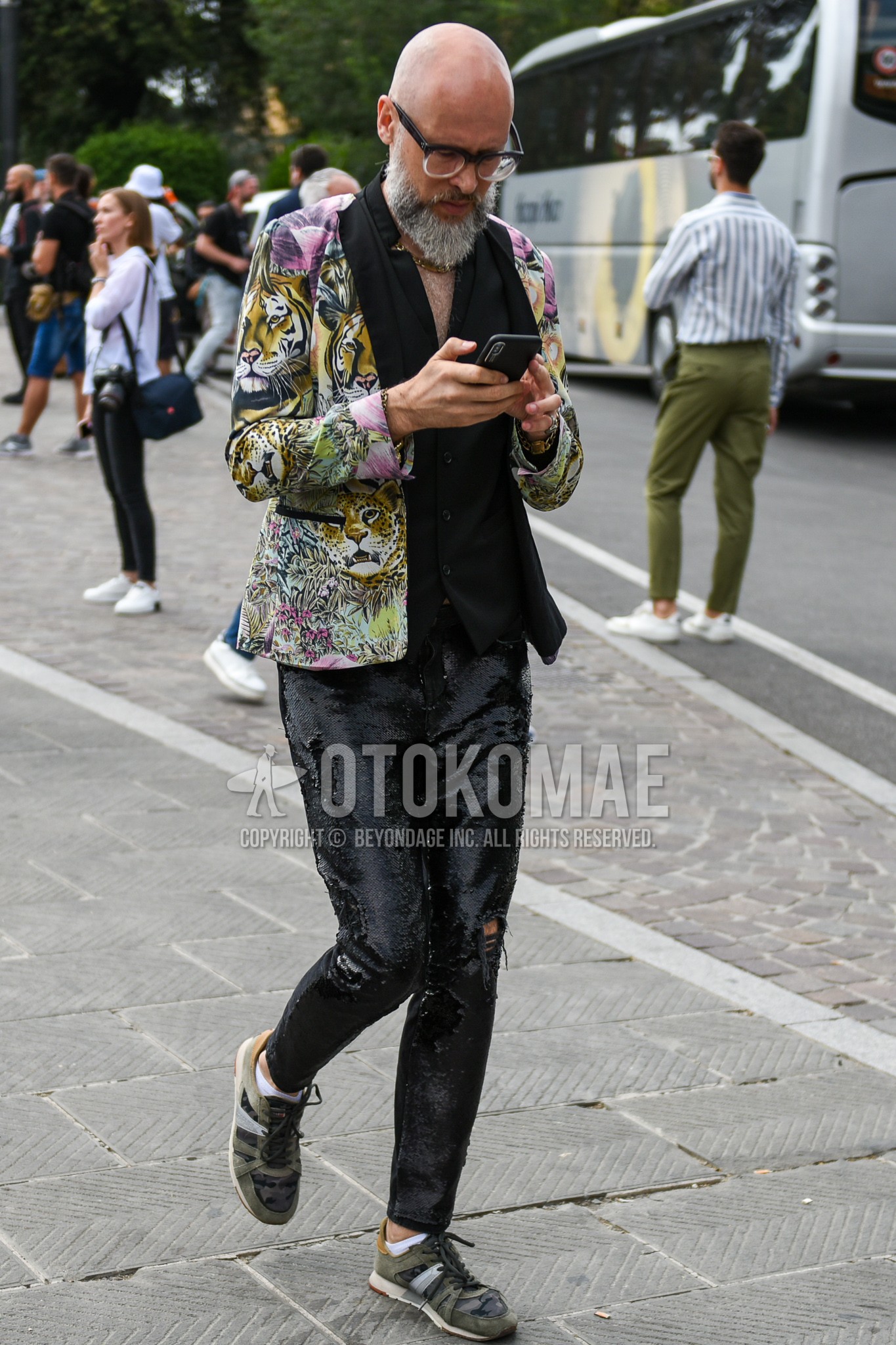 Men's spring summer autumn outfit with black clear plain sunglasses, multi-color outerwear tailored jacket, black plain gilet, black plain shirt, black plain bottoms, olive green low-cut sneakers.
