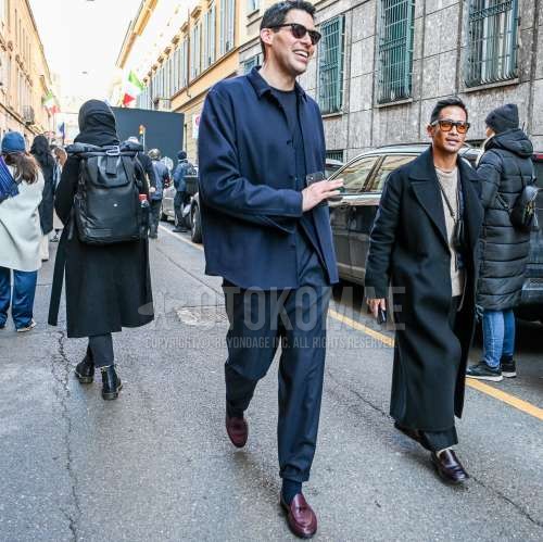 黒無地のサングラス、ブルー無地のシャツジャケット、ネイビー無地のセーター、ブルー無地のスラックス、ネイビー無地のソックス、パープルローファーの革靴を合わせた秋春のメンズコーデ・着こなし。