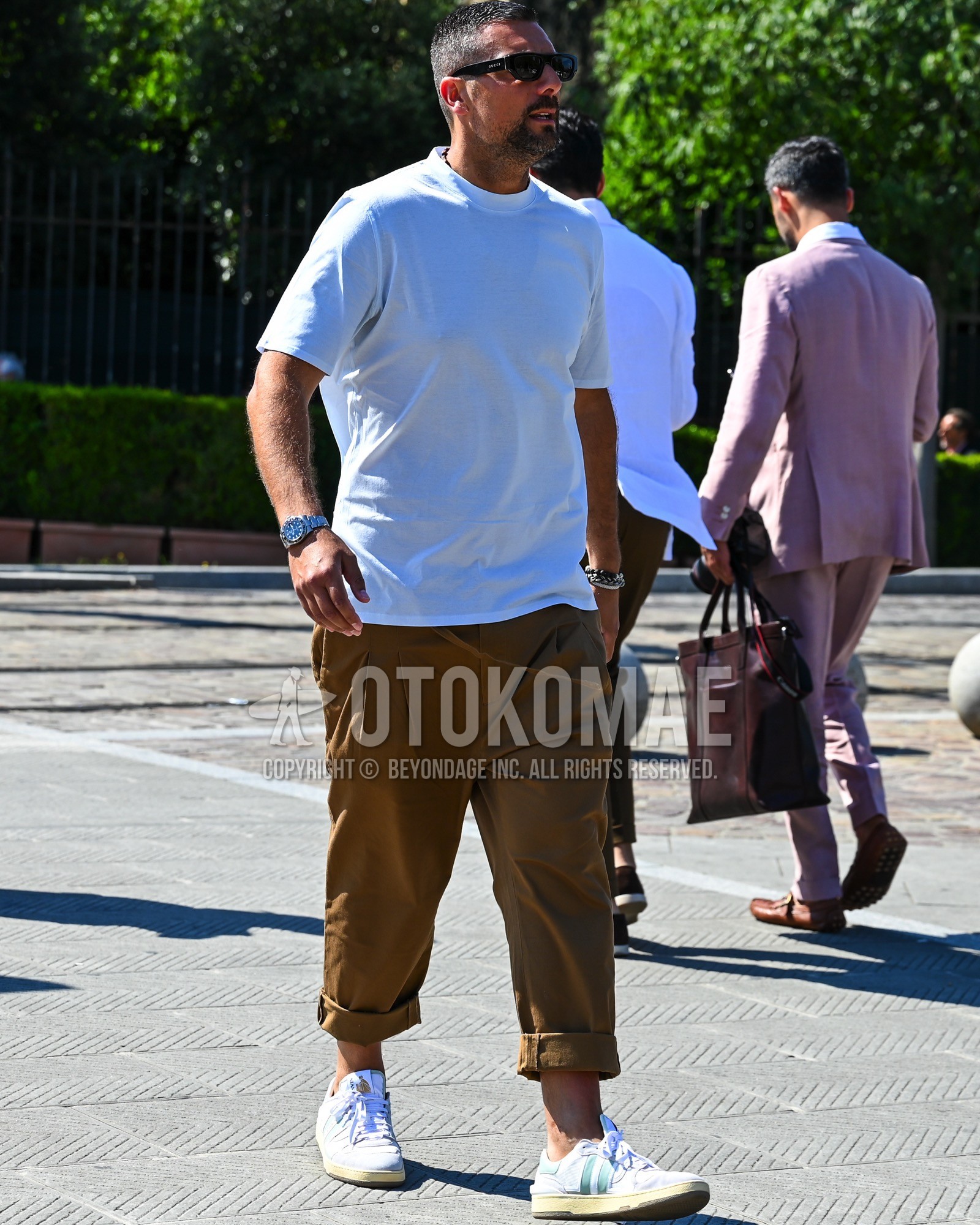 Men's spring summer outfit with black plain sunglasses, white plain t-shirt, brown plain chinos, white low-cut sneakers.