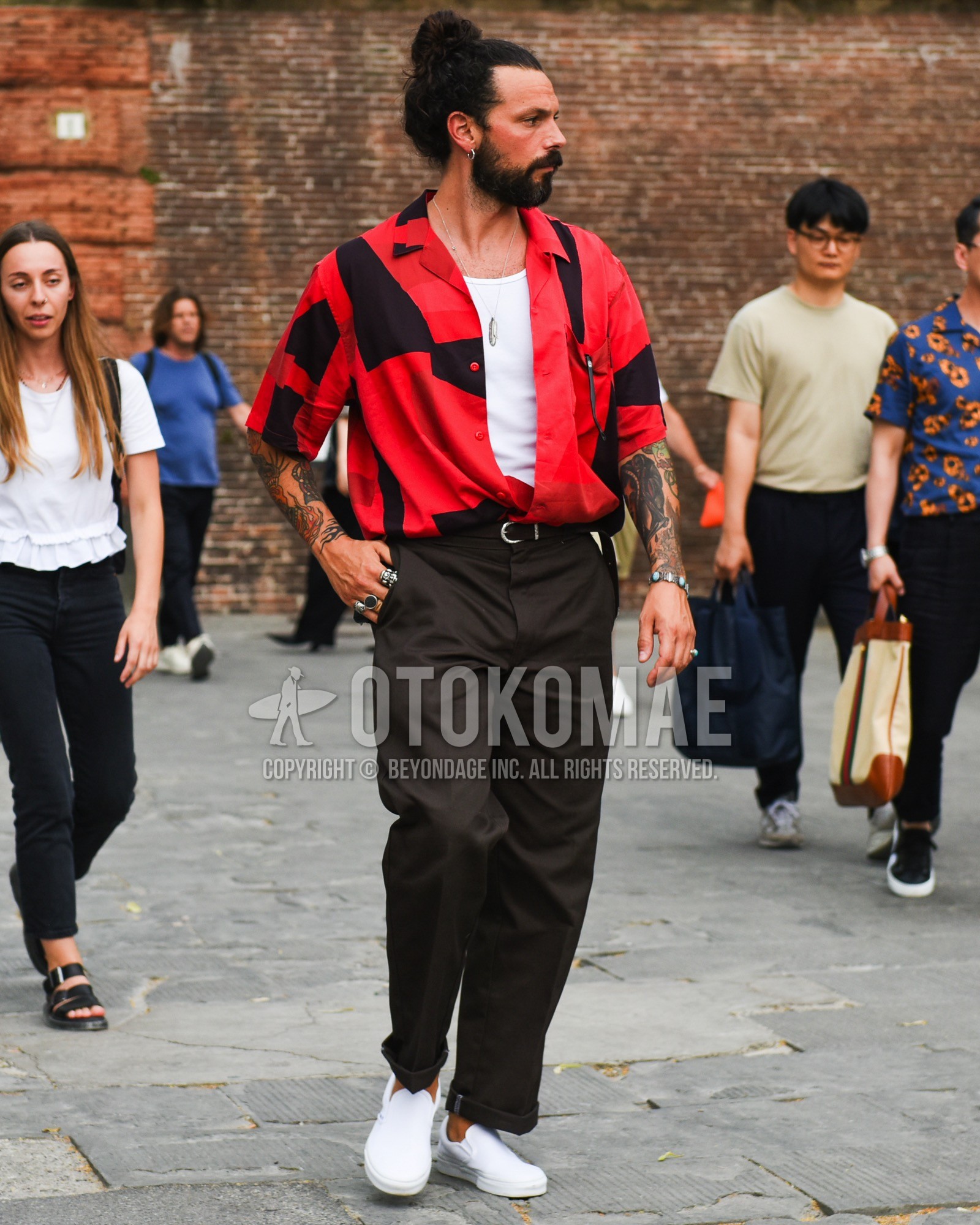 Men's spring summer outfit with white plain tank top, red graphic shirt, brown plain leather belt, brown plain slacks, white low-cut sneakers.