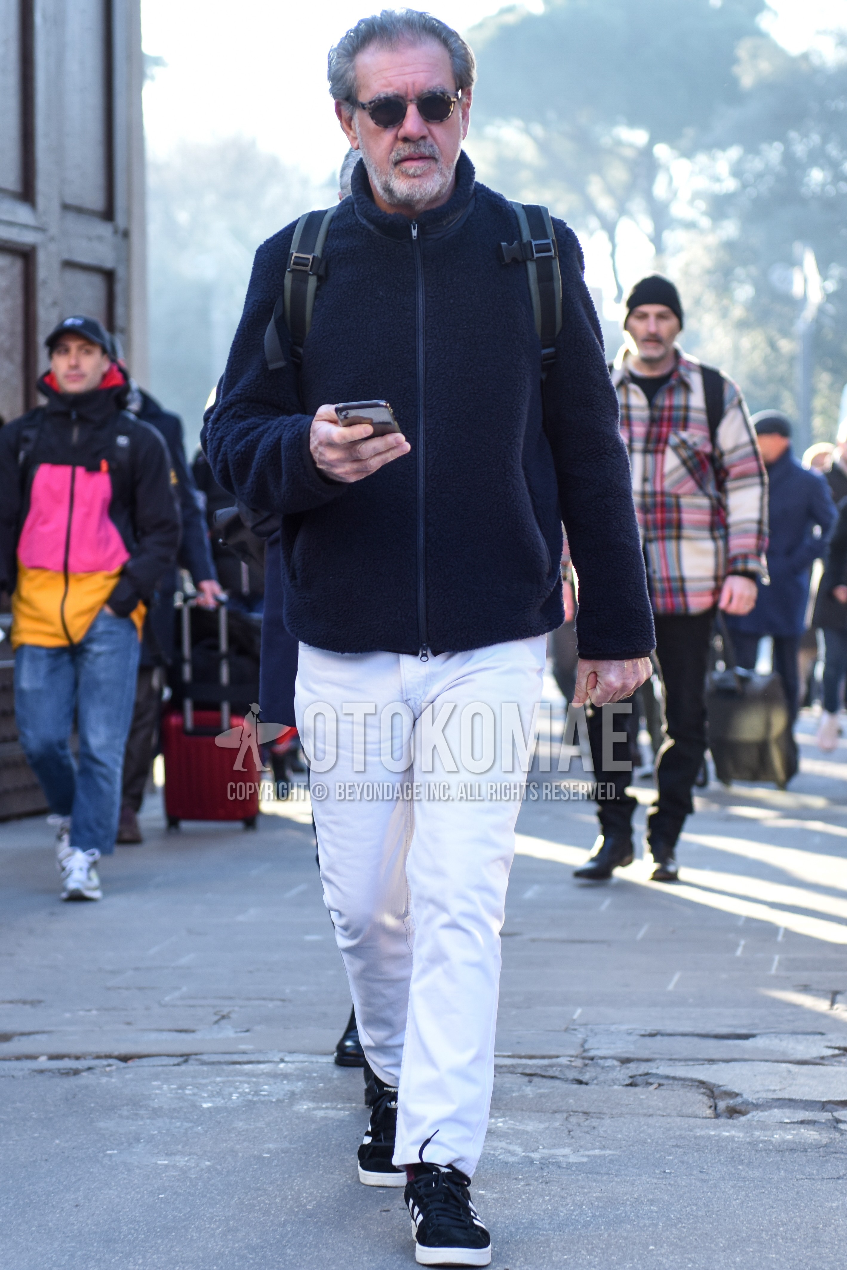 Men's autumn winter outfit with dark gray tortoiseshell sunglasses, black plain fleece jacket, white plain cotton pants, white plain ankle pants, black low-cut sneakers.