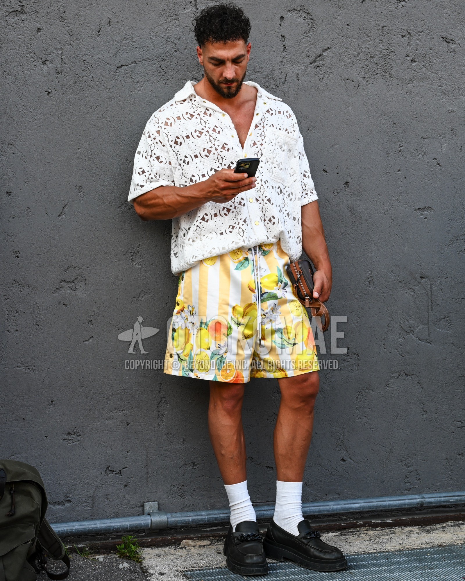 Men's spring summer outfit with white plain polo shirt, yellow whole pattern short pants, white plain socks, black coin loafers leather shoes.