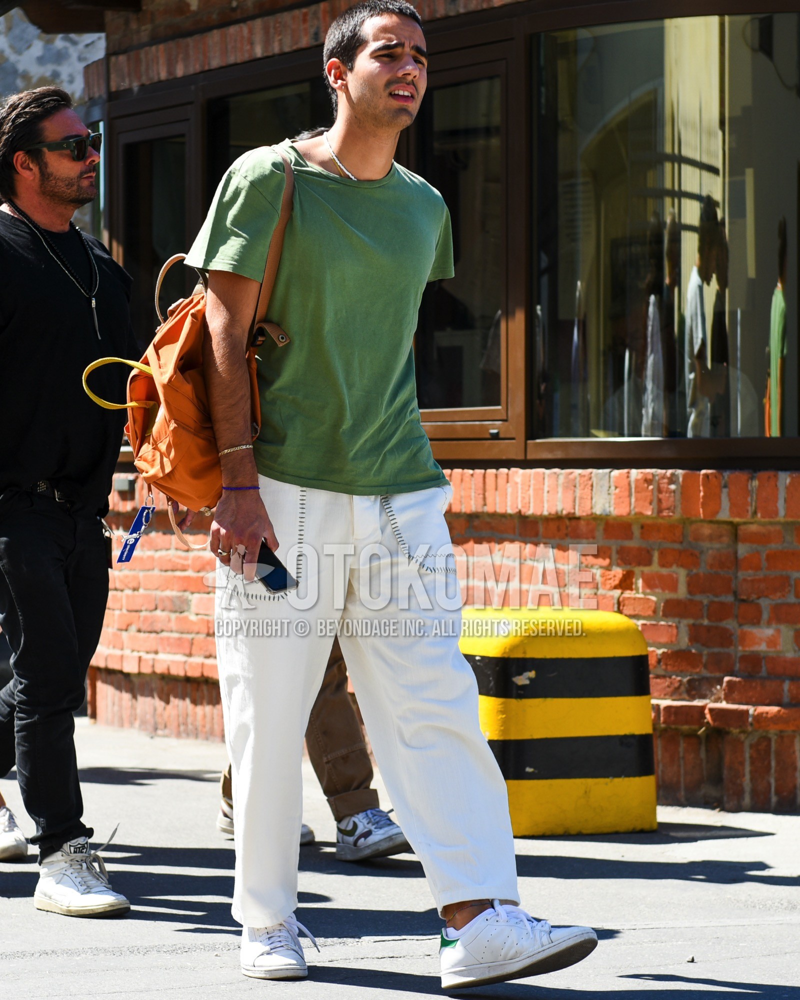 Men's spring summer outfit with green plain t-shirt, white plain cotton pants, white low-cut sneakers, orange plain bag.