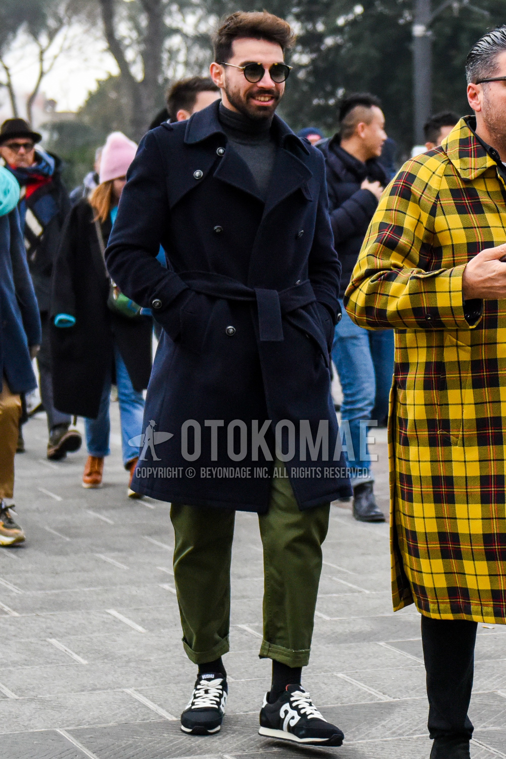 Men's winter outfit with black tortoiseshell sunglasses, navy plain trench coat, dark gray plain turtleneck knit, olive green plain chinos, black plain socks, black low-cut sneakers.