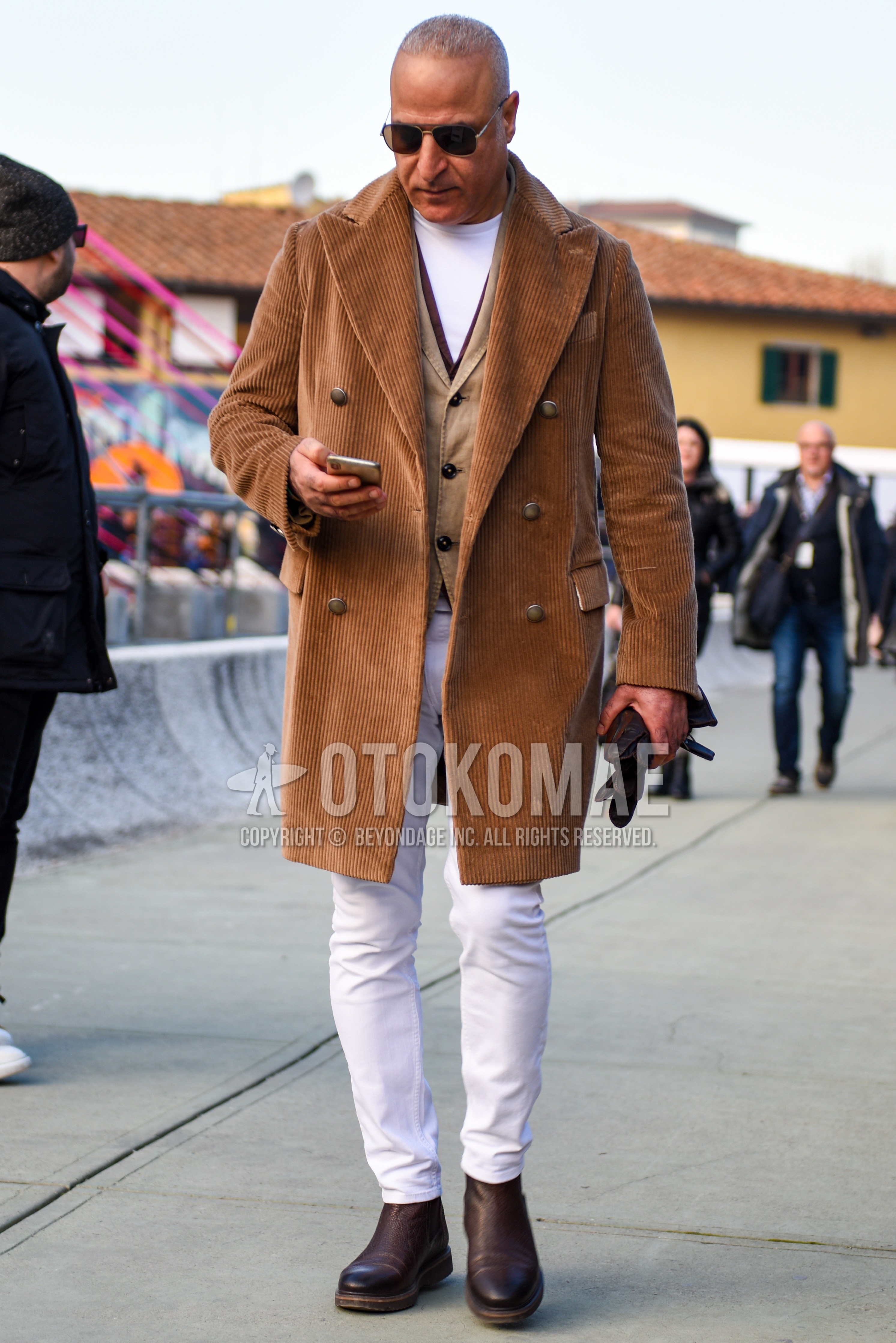 Men's autumn winter outfit with silver plain sunglasses, brown plain chester coat, beige plain gilet, white plain t-shirt, white plain cotton pants, brown side-gore boots.