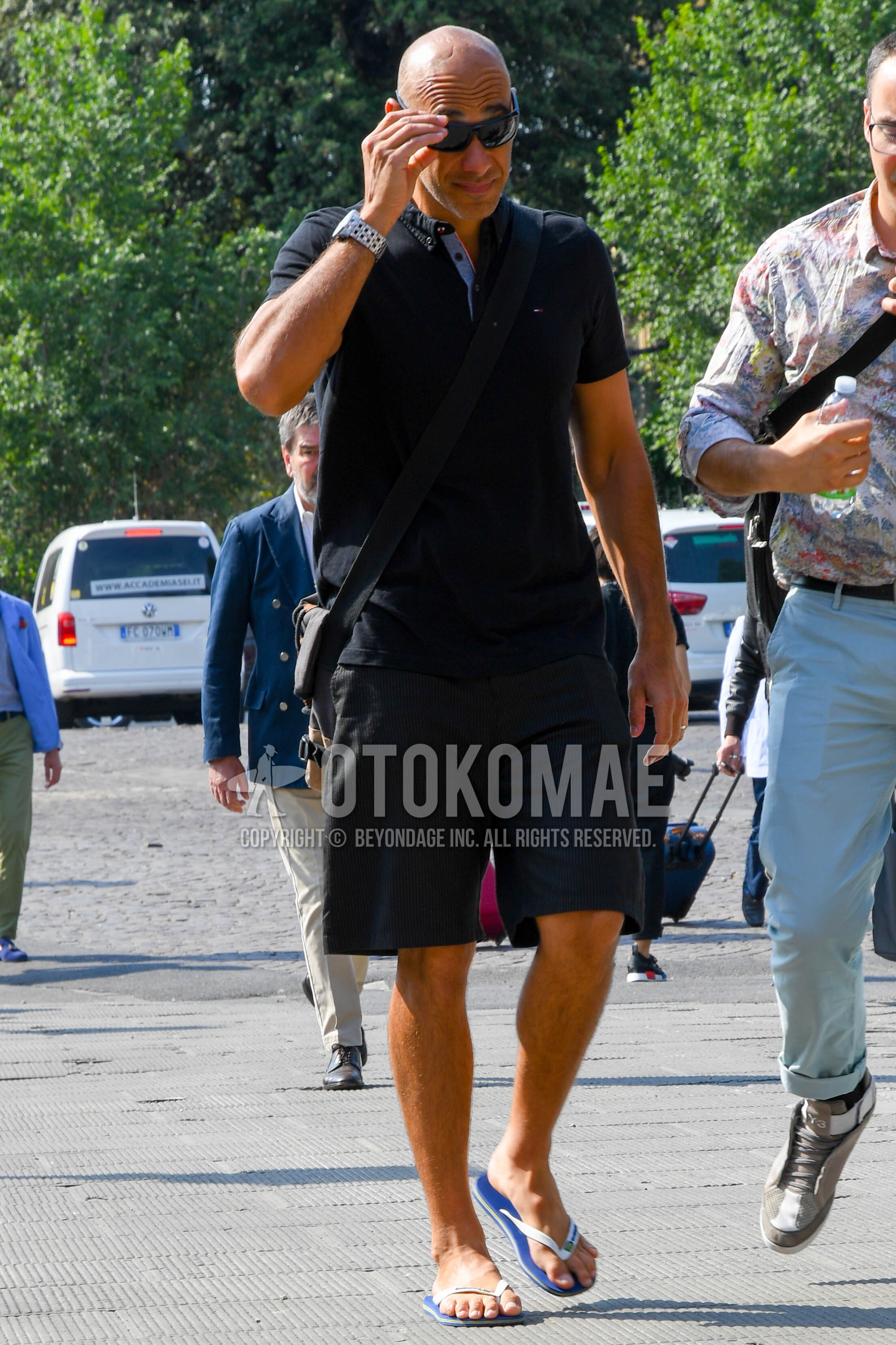 Men's summer outfit with plain sunglasses, black plain polo shirt, black plain short pants, white blue flip flops sandals.