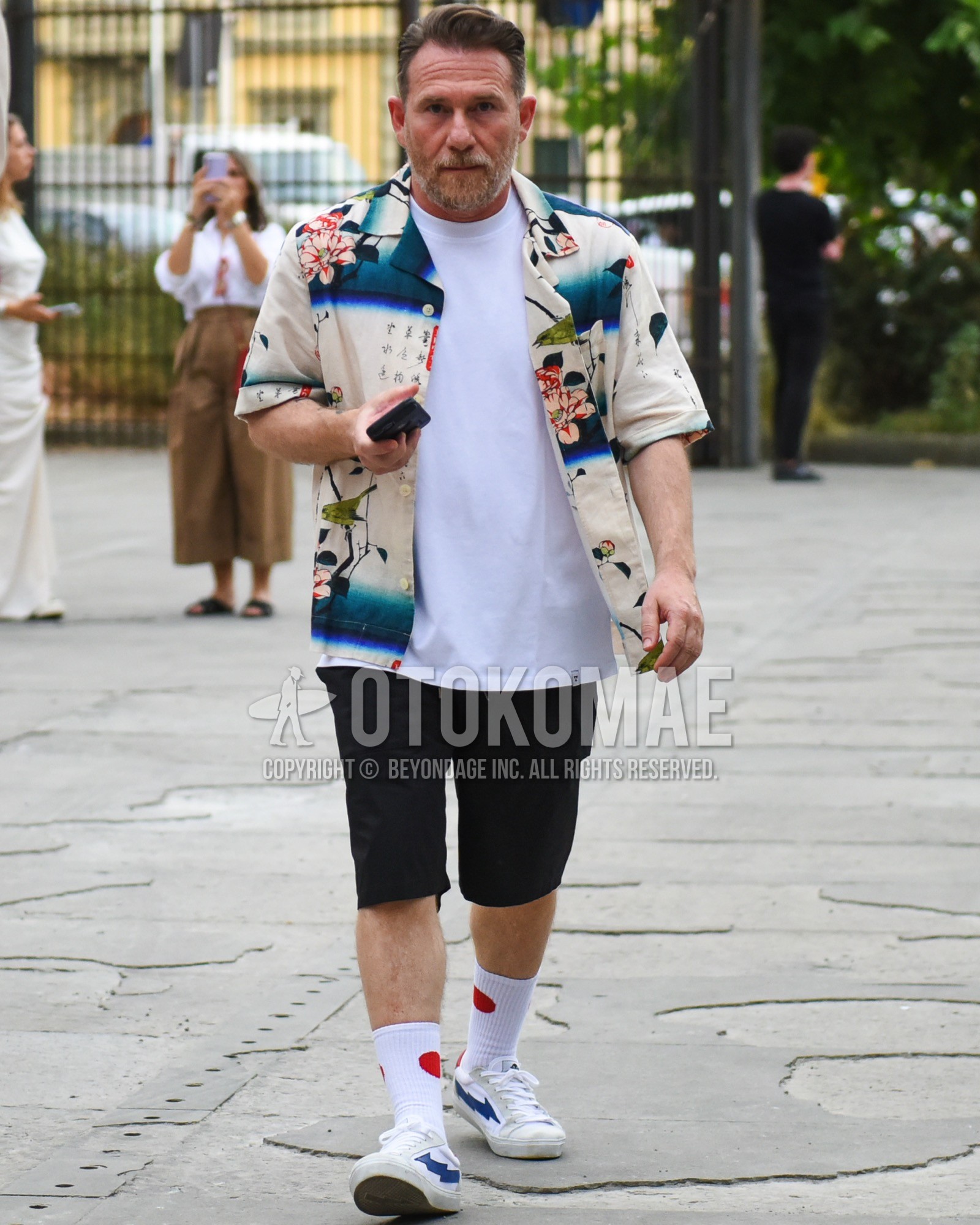 Men's spring summer outfit with beige graphic shirt, white plain t-shirt, black plain short pants, white one point socks, white low-cut sneakers.