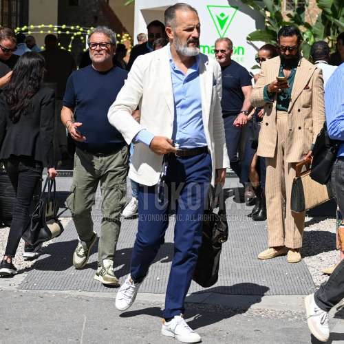 白無地のテーラードジャケット、水色無地のシャツ、黒無地のレザーベルト、ブルー無地のスラックス、黒無地のソックス、白ローカットのスニーカー、黒無地のクラッチバッグ/セカンドバッグ/巾着を合わせた秋春のメンズコーデ・着こなし。