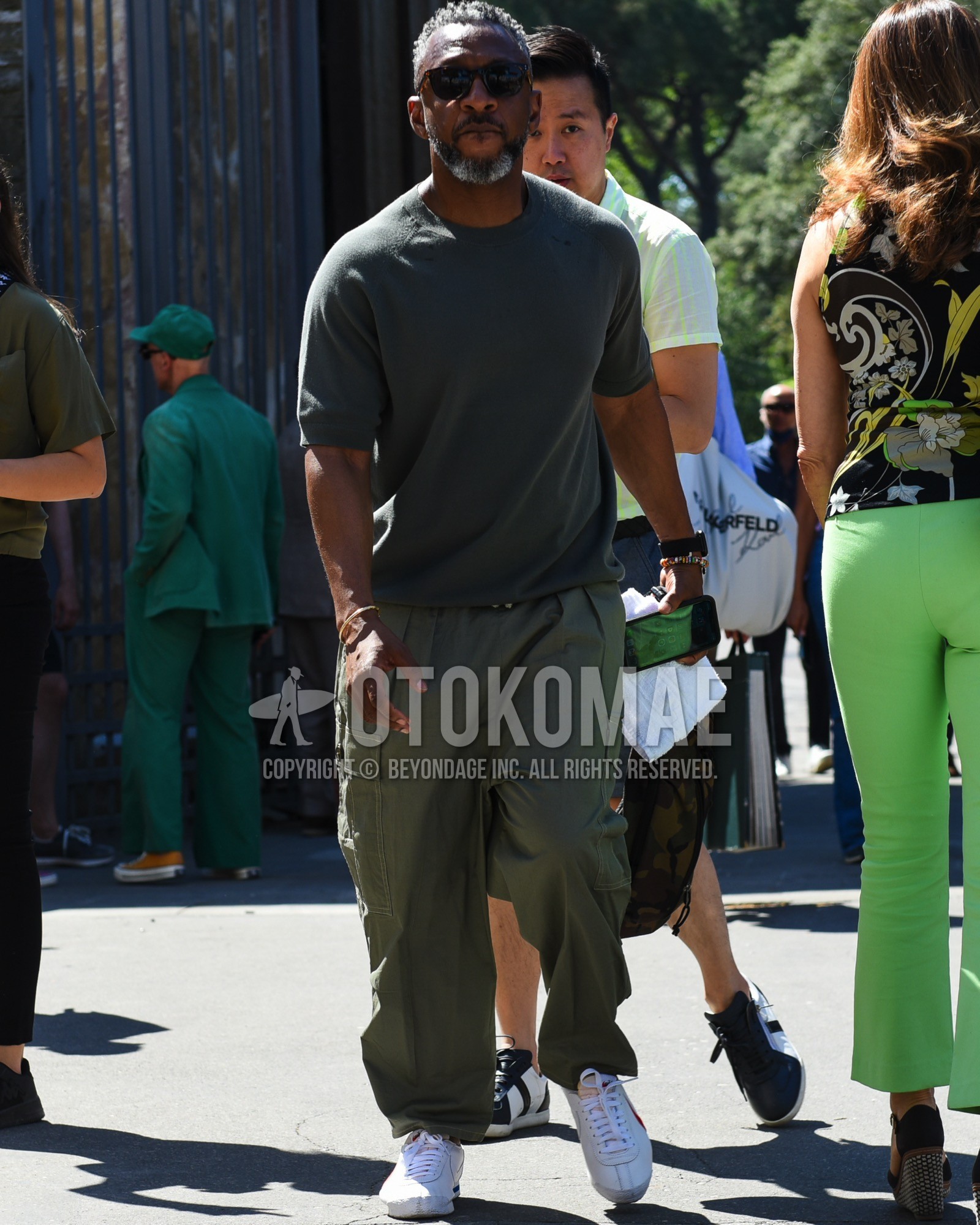 Men's spring summer outfit with brown tortoiseshell sunglasses, olive green plain t-shirt, olive green plain cargo pants, white low-cut sneakers.
