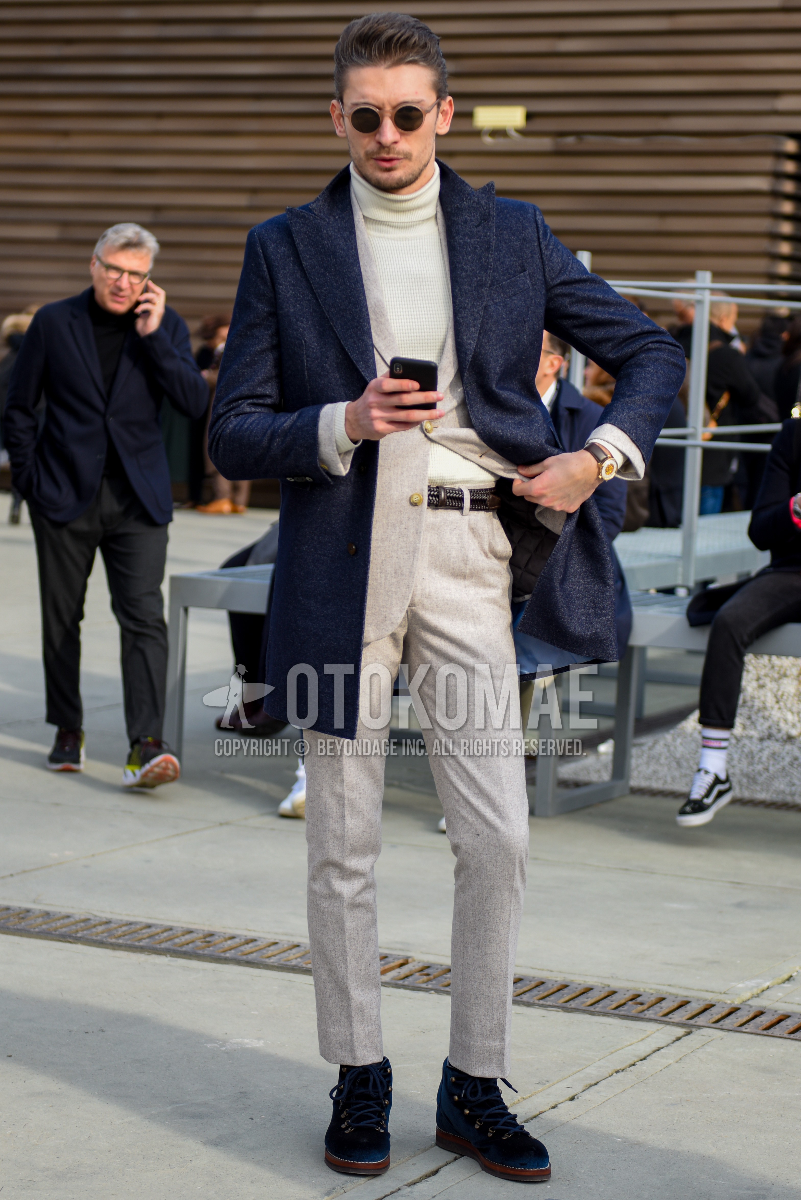 Men's winter outfit with beige plain sunglasses, navy plain chester coat, white plain turtleneck knit, black plain leather belt, black  boots, beige plain suit.