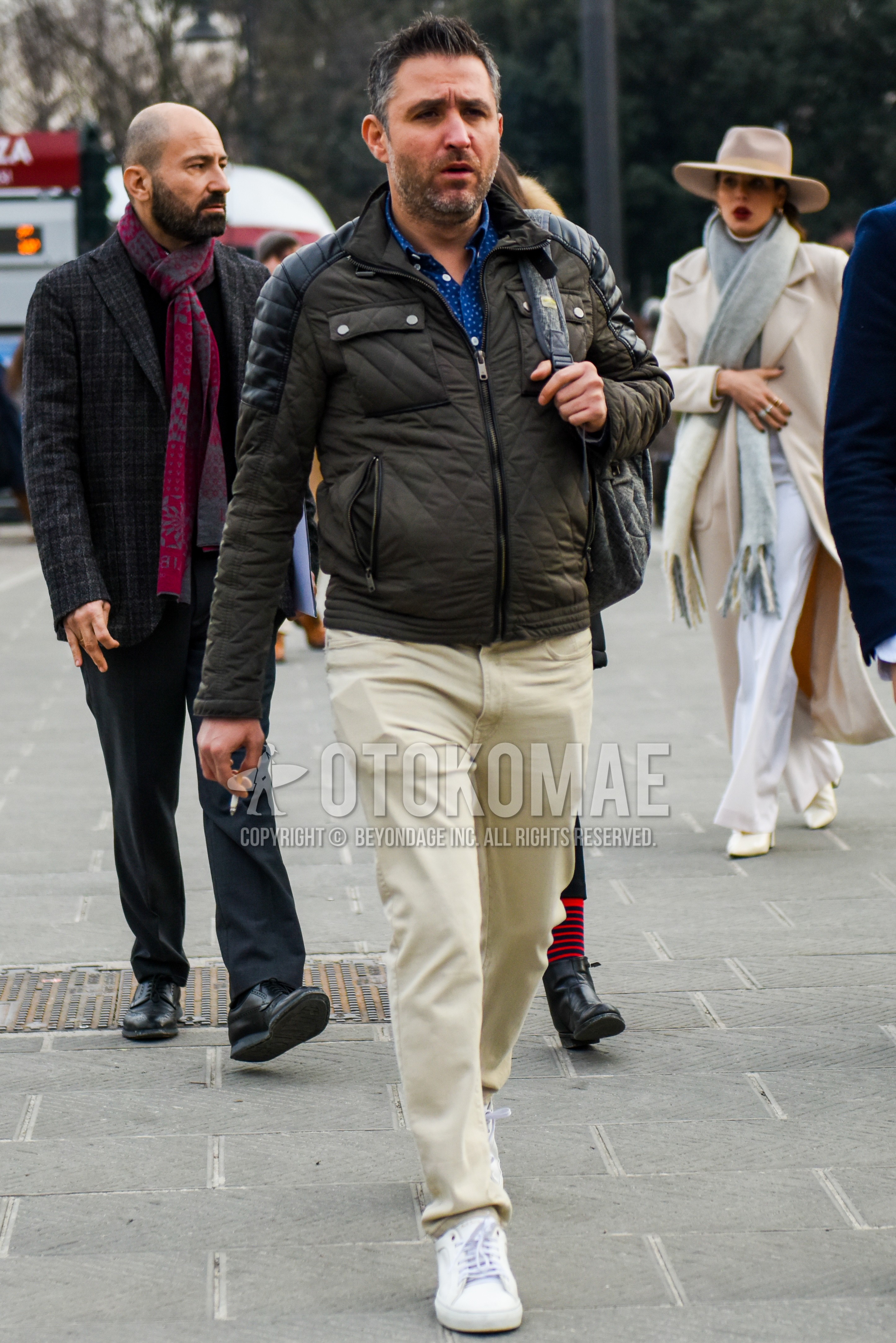 Men's winter outfit with olive green plain quilted jacket, blue plain shirt, white plain cotton pants, white sneakers.