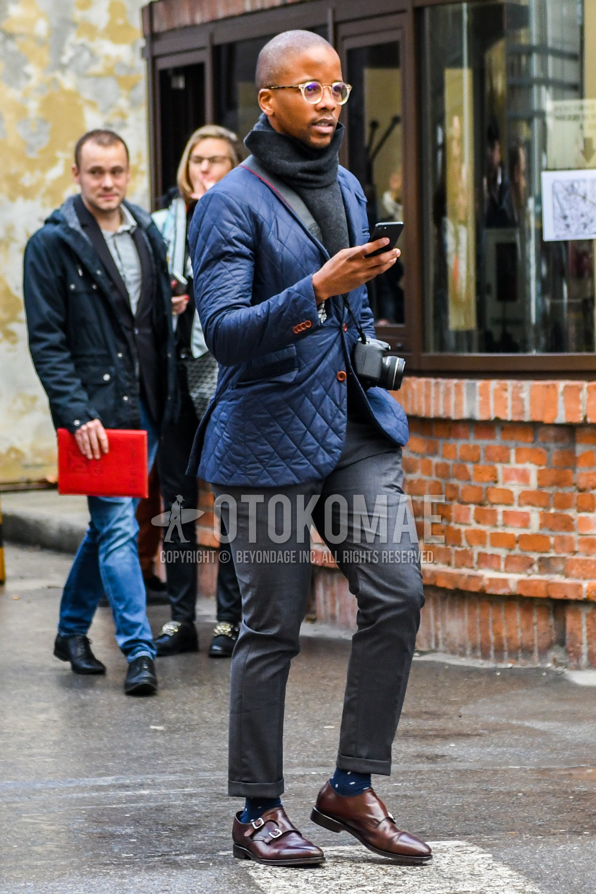 Men's winter outfit with plain glasses, dark gray plain scarf, blue plain quilted jacket, dark gray plain slacks, navy dots socks, brown monk shoes leather shoes.