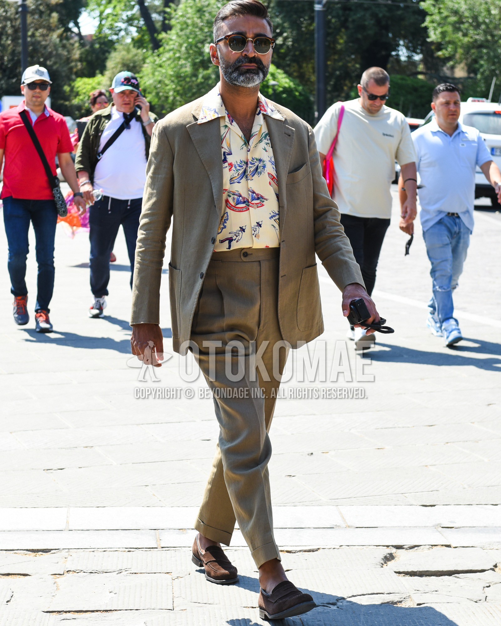 Men's spring summer outfit with brown plain sunglasses, beige graphic shirt, brown coin loafers leather shoes, brown suede shoes leather shoes, brown plain suit.