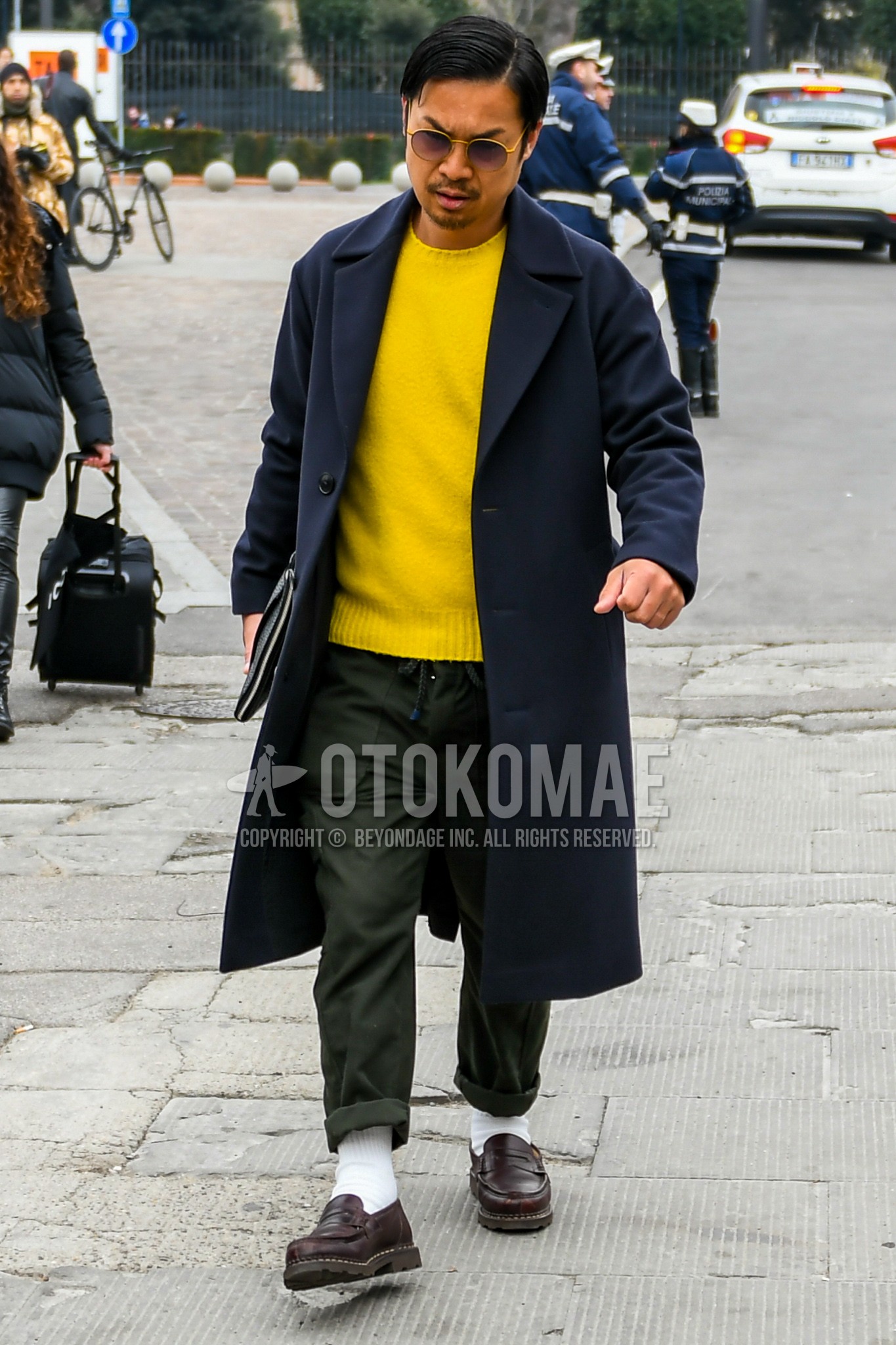 Men's winter outfit with gold plain sunglasses, navy plain chester coat, yellow plain sweater, olive green plain easy pants, white plain socks, brown coin loafers leather shoes, black plain clutch bag/second bag/drawstring bag.