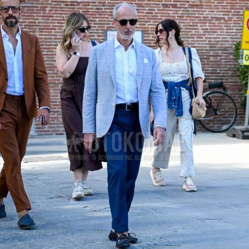 黒無地のサングラス、グレー無地のテーラードジャケット、白無地のシャツ、黒無地のレザーベルト、ブルー無地のスラックス、黒の革靴を合わせた春秋のメンズコーデ・着こなし。