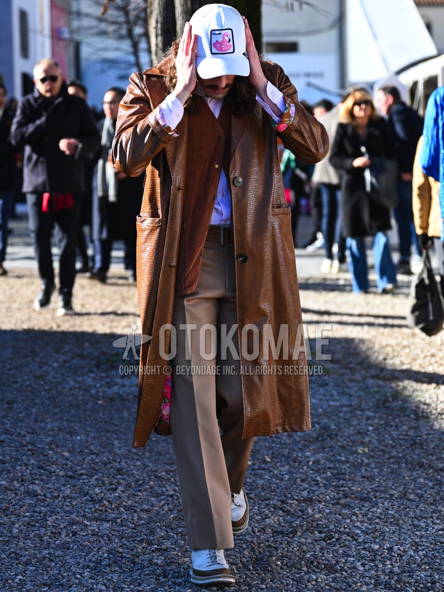 Men's autumn winter outfit with white pink one point baseball cap, brown plain ulster coat, brown plain outerwear, brown plain quilted jacket, pink plain shirt, brown plain leather belt, beige plain slacks, white brown low-cut sneakers.