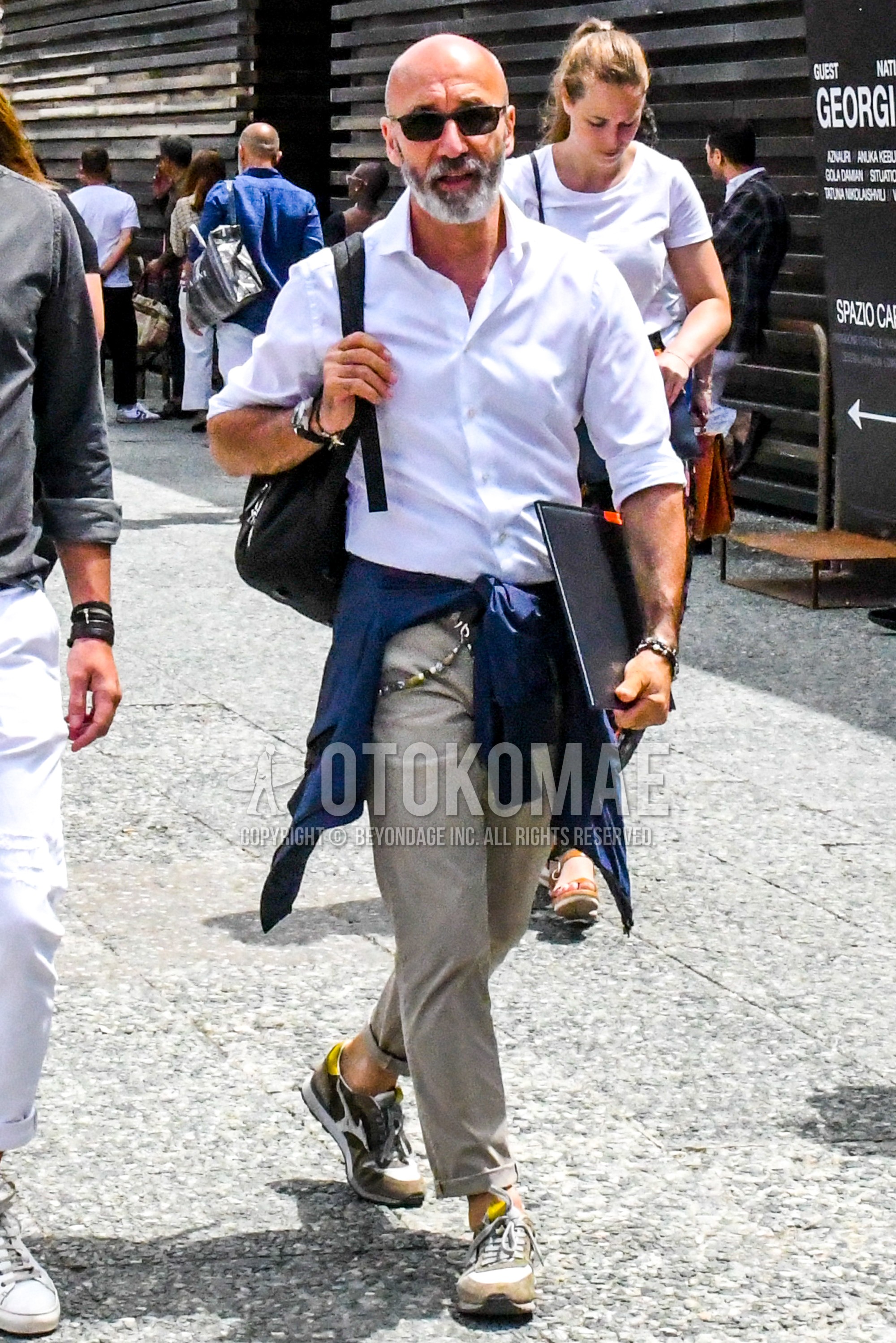 Men's summer outfit with black plain sunglasses, white plain shirt, beige plain chinos, beige low-cut sneakers, black plain backpack.