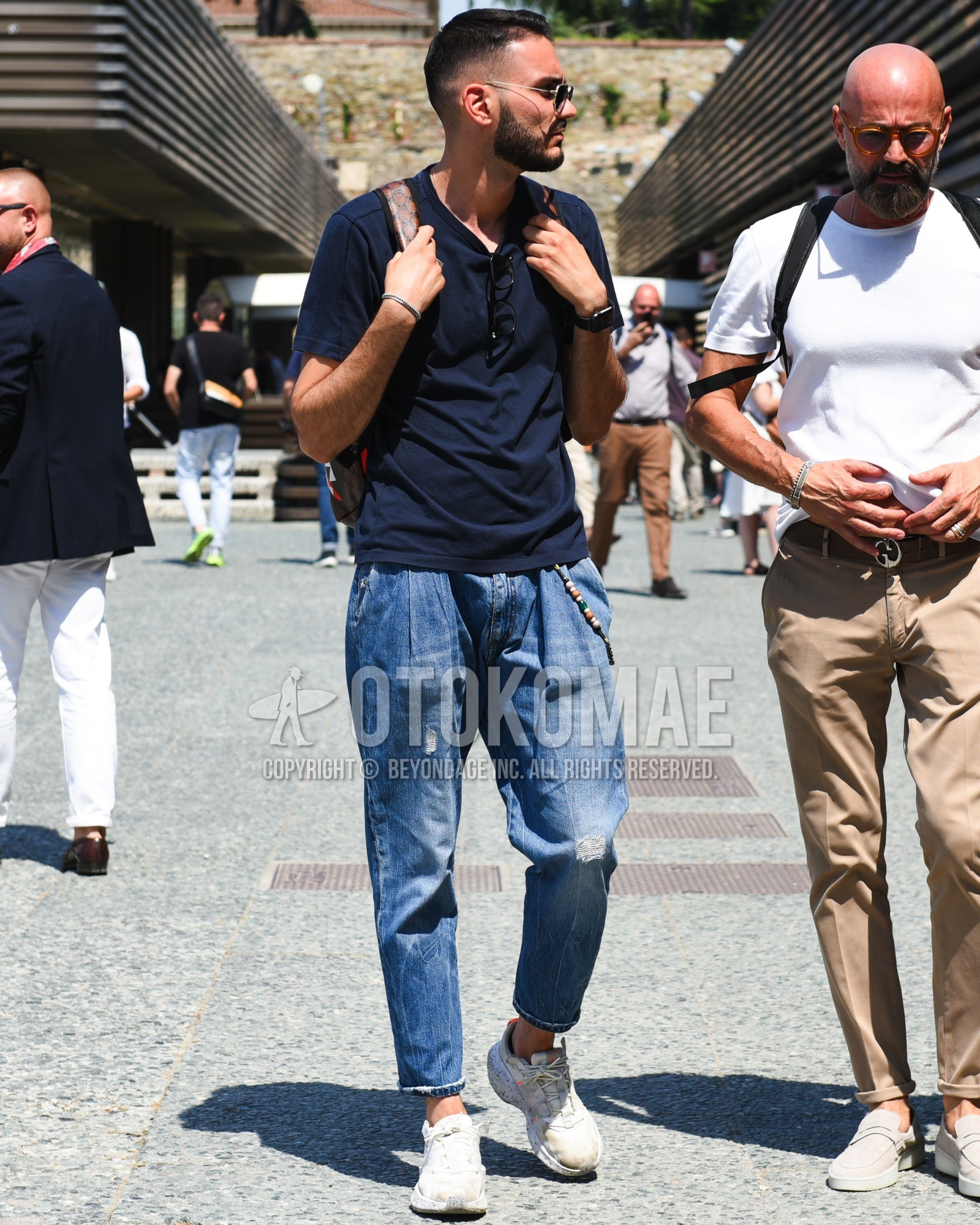 Men's spring summer outfit with gold plain sunglasses, navy plain t-shirt, blue plain denim/jeans, blue plain cropped pants, blue plain damaged jeans, white low-cut sneakers, brown dots backpack.
