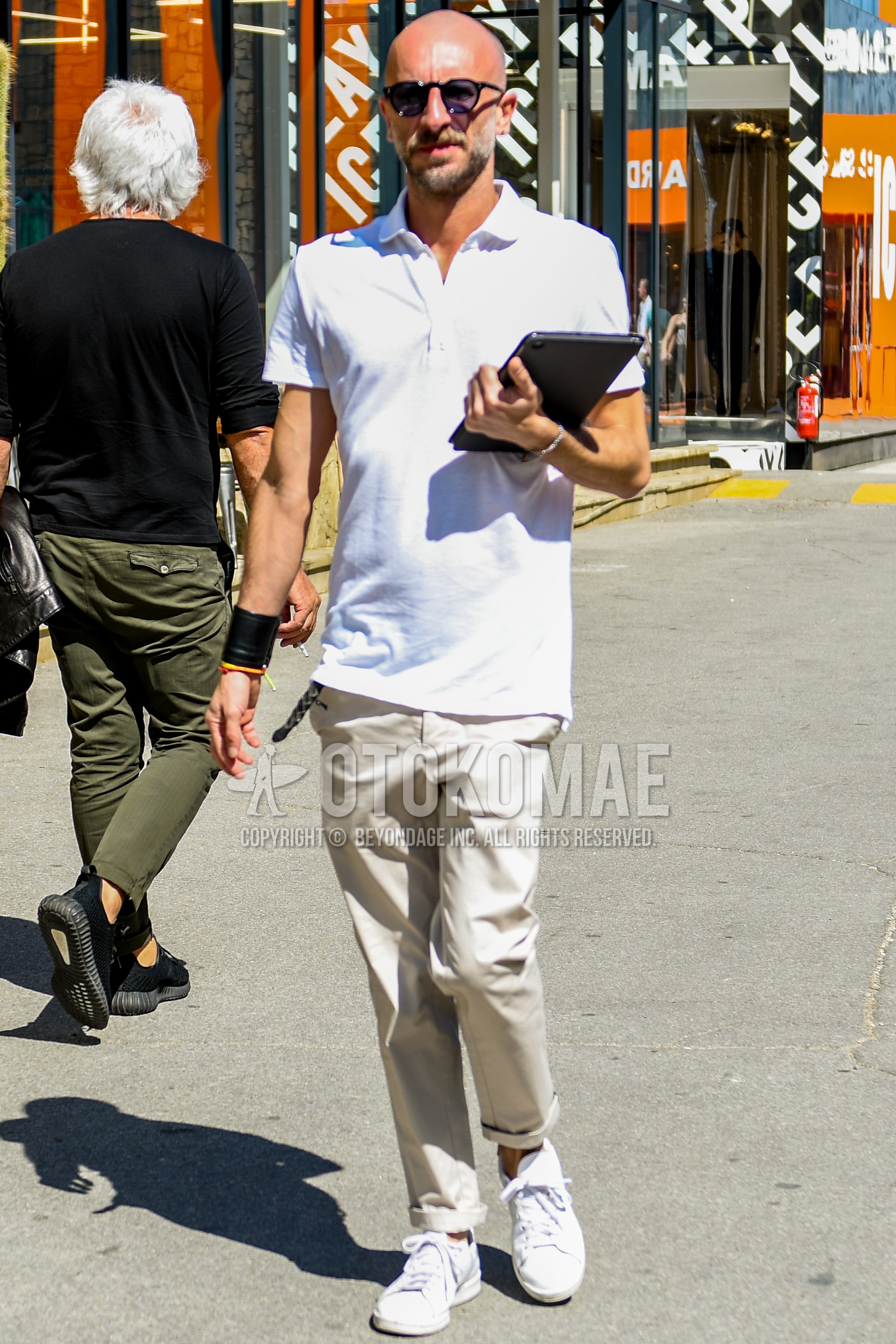 Men's spring summer outfit with black plain sunglasses, white plain polo shirt, beige plain chinos, white low-cut sneakers.