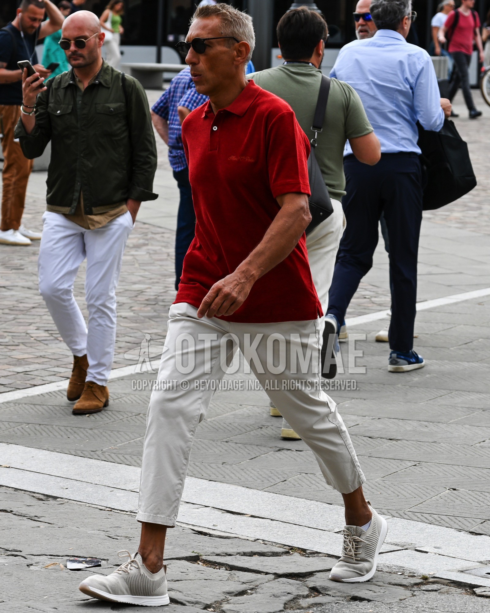 Men's spring summer outfit with black tortoiseshell sunglasses, red plain polo shirt, white plain chinos, white low-cut sneakers.
