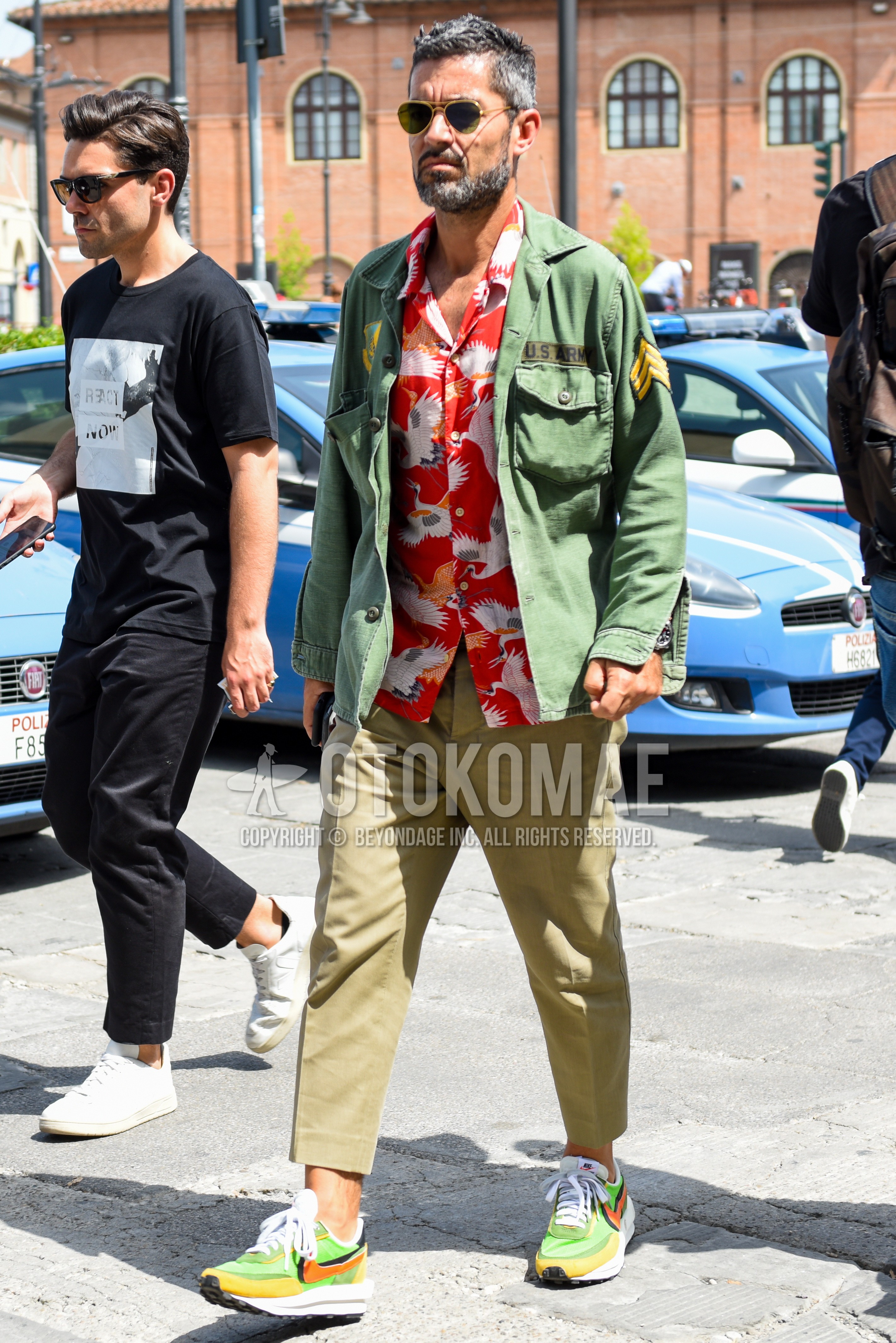 Men's spring summer autumn outfit with gold plain sunglasses, green plain safari jacket, red tops/innerwear shirt, beige plain ankle pants, green low-cut sneakers.