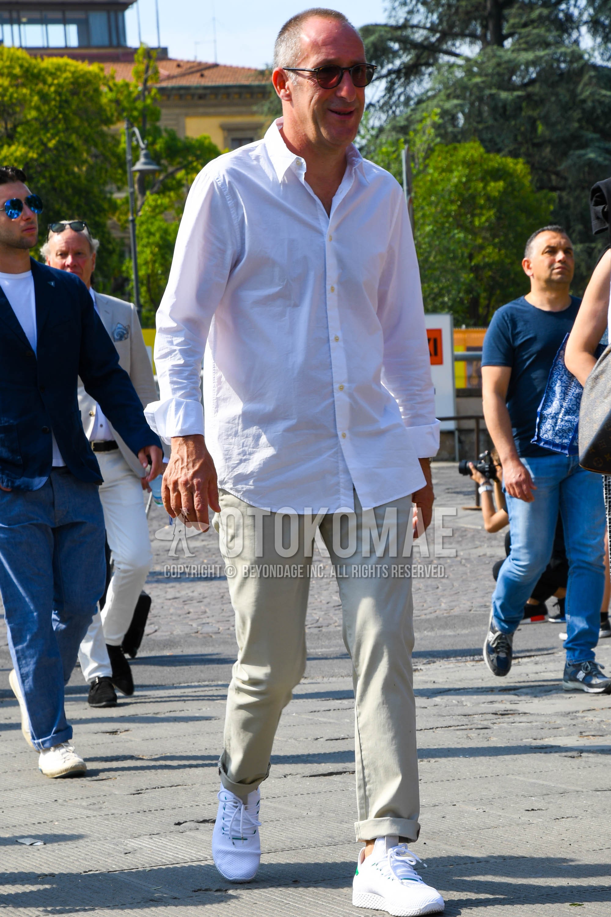 Men's spring summer outfit with brown plain sunglasses, white plain shirt, beige plain chinos, white low-cut sneakers.