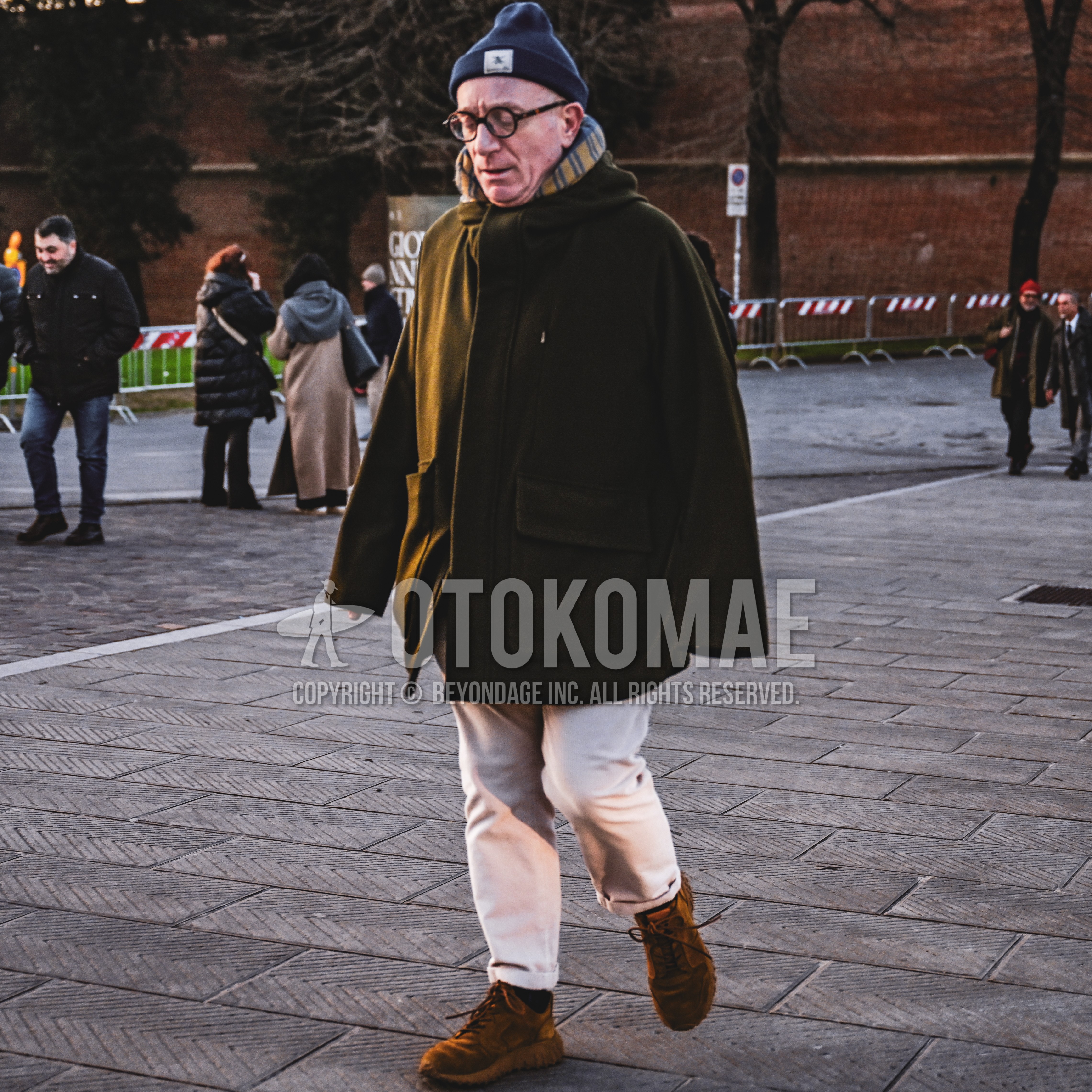 Men's autumn winter outfit with dark gray one point knit cap, brown tortoiseshell glasses, gray yellow horizontal stripes scarf, olive green plain hooded coat, beige plain winter pants (corduroy,velour), brown low-cut sneakers.