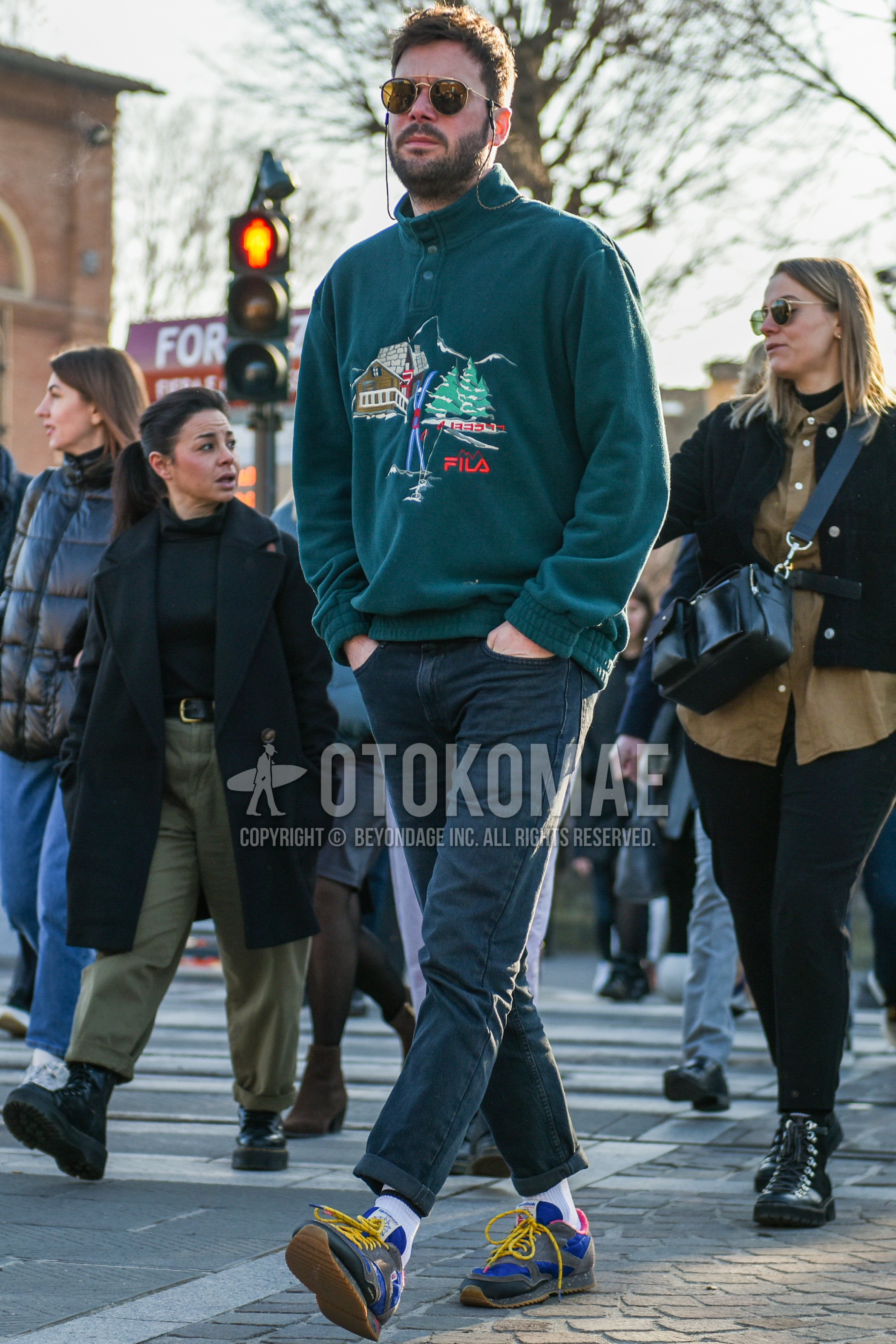 Men's autumn winter outfit with black plain sunglasses, green plain fleece jacket, dark gray plain denim/jeans, white plain socks, blue gray low-cut sneakers.