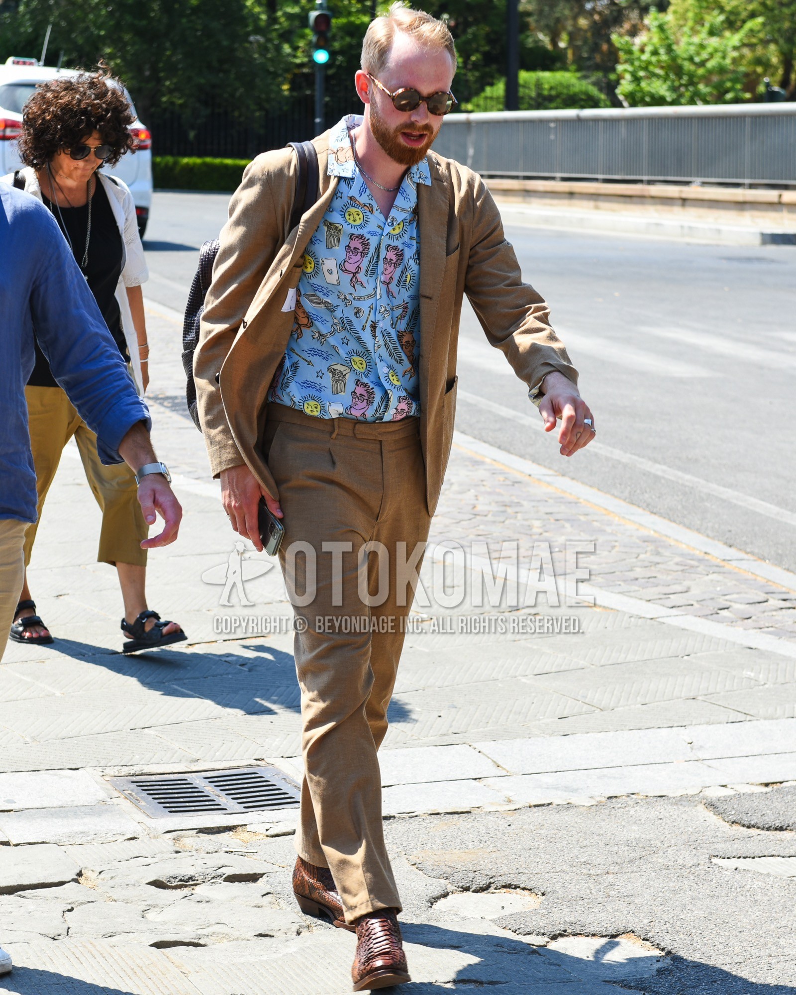 Men's spring summer outfit with brown tortoiseshell sunglasses, blue graphic shirt, brown  boots, brown plain backpack, brown plain suit.