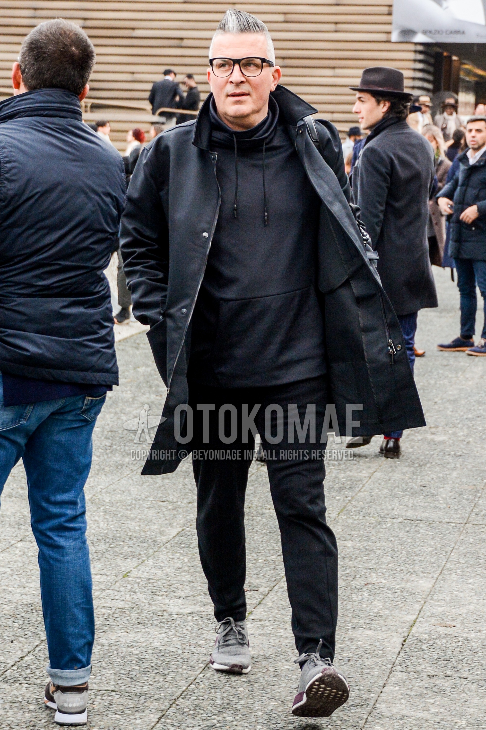 Men's winter outfit with black plain glasses, black plain stenkarrer coat, black plain hoodie, dark gray plain slacks, gray low-cut sneakers.