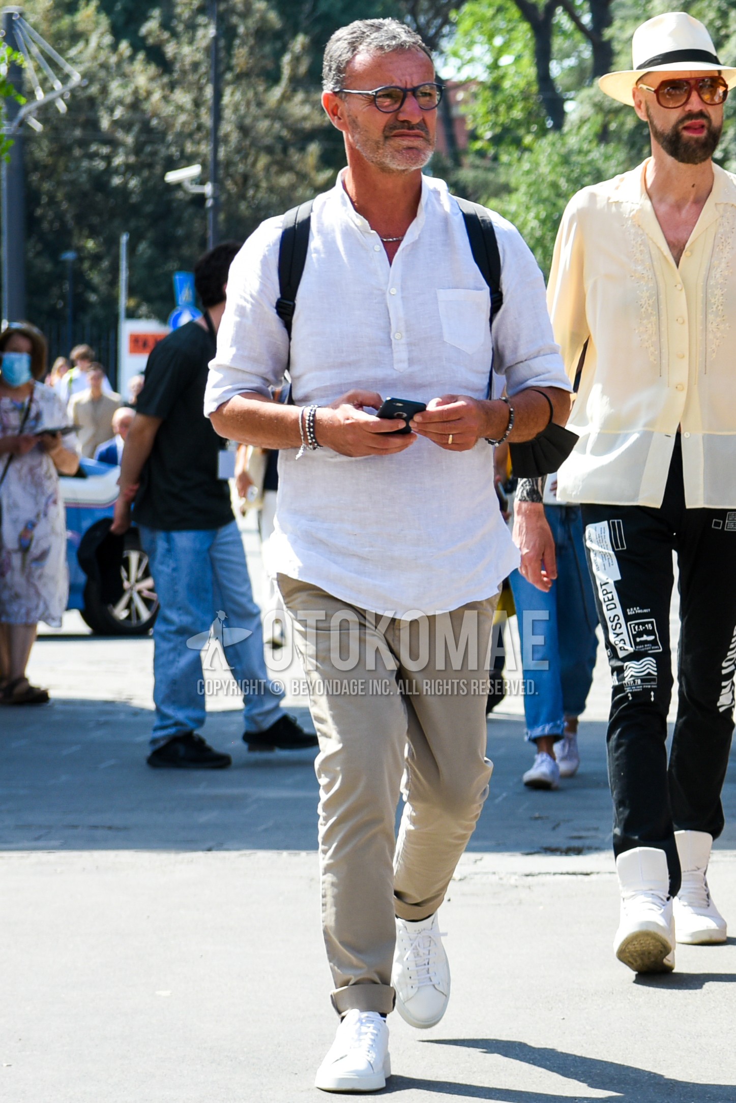 Men's spring summer outfit with black plain glasses, white plain shirt, beige plain chinos, white low-cut sneakers.