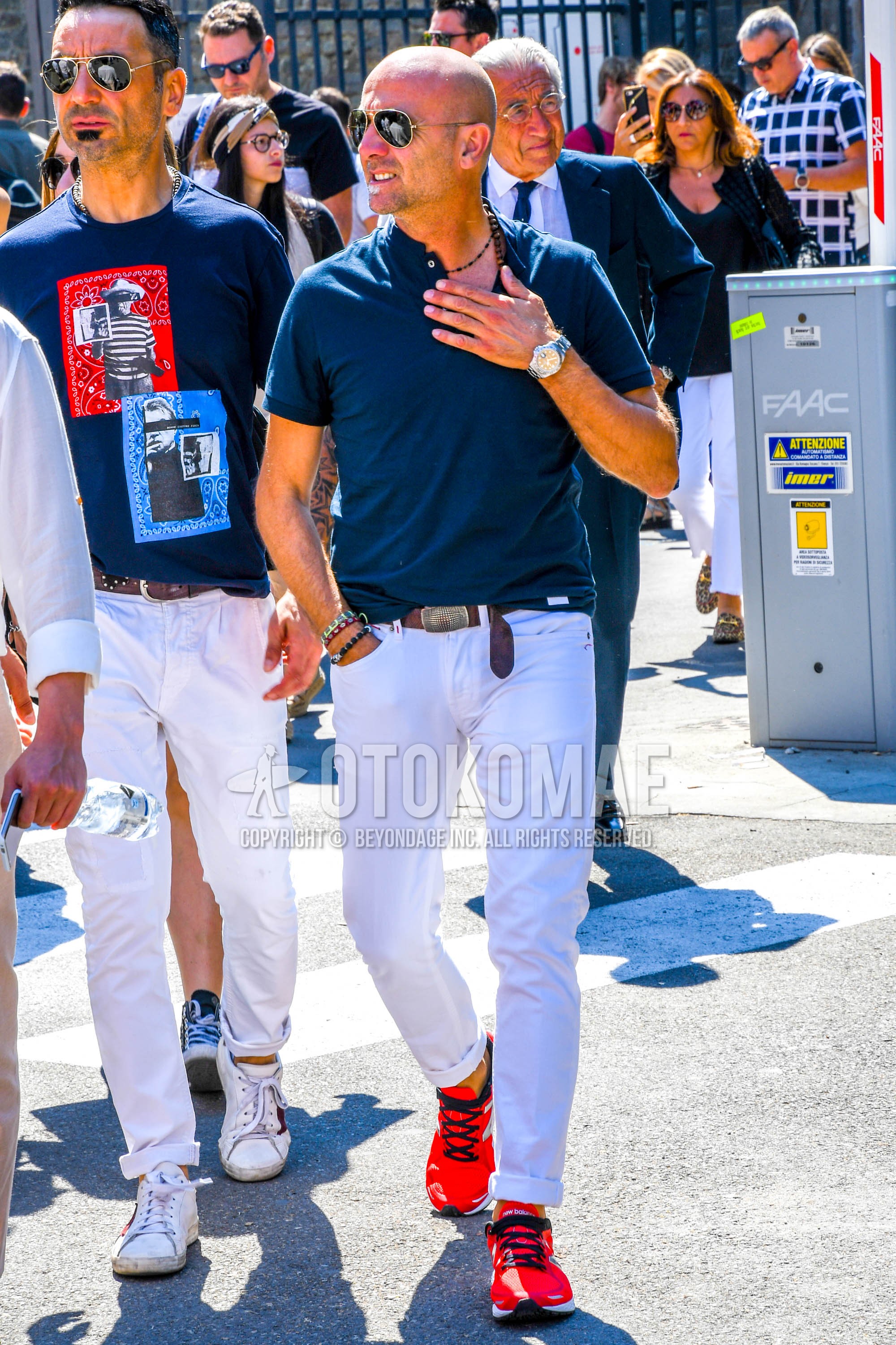 Men's spring summer outfit with silver plain sunglasses, blue plain polo shirt, brown plain leather belt, white plain cotton pants, red low-cut sneakers.