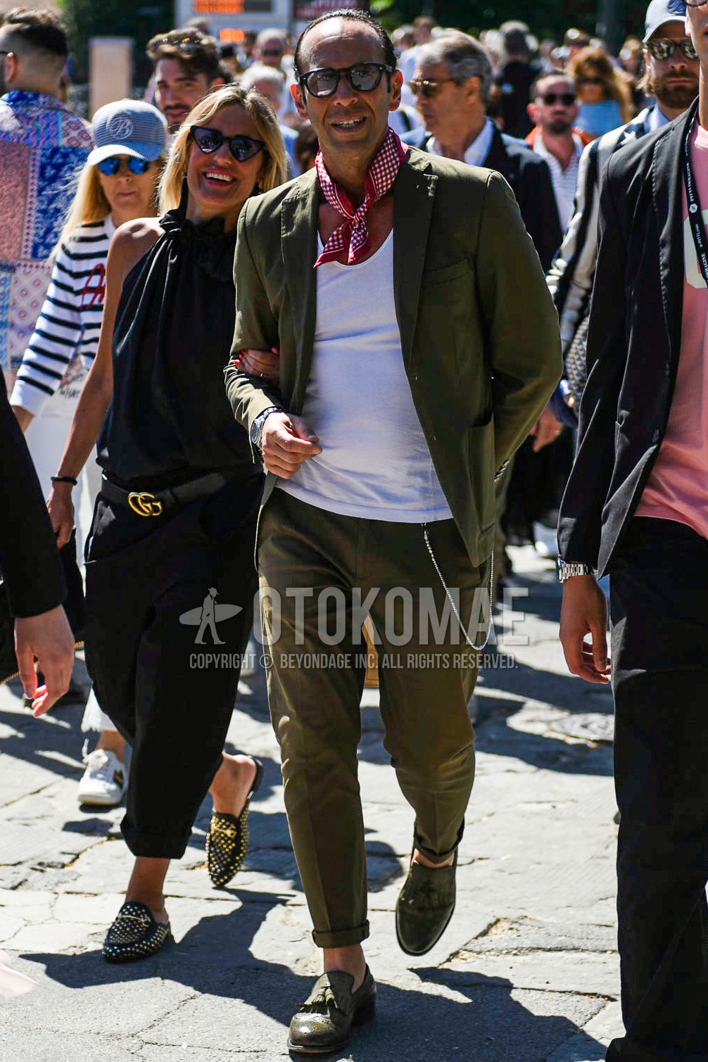 Men's spring summer outfit with black plain sunglasses, red dots bandana/neckerchief, white plain t-shirt, olive green tassel loafers leather shoes, olive green plain suit.