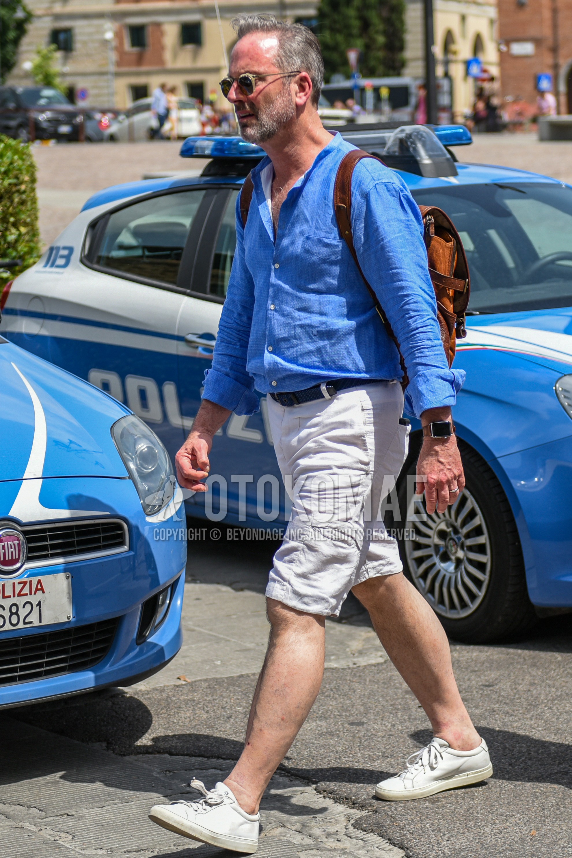 Men's spring summer outfit with beige plain sunglasses, light blue plain shirt, blue plain braided belt, white plain cargo pants, white plain short pants, white low-cut sneakers.