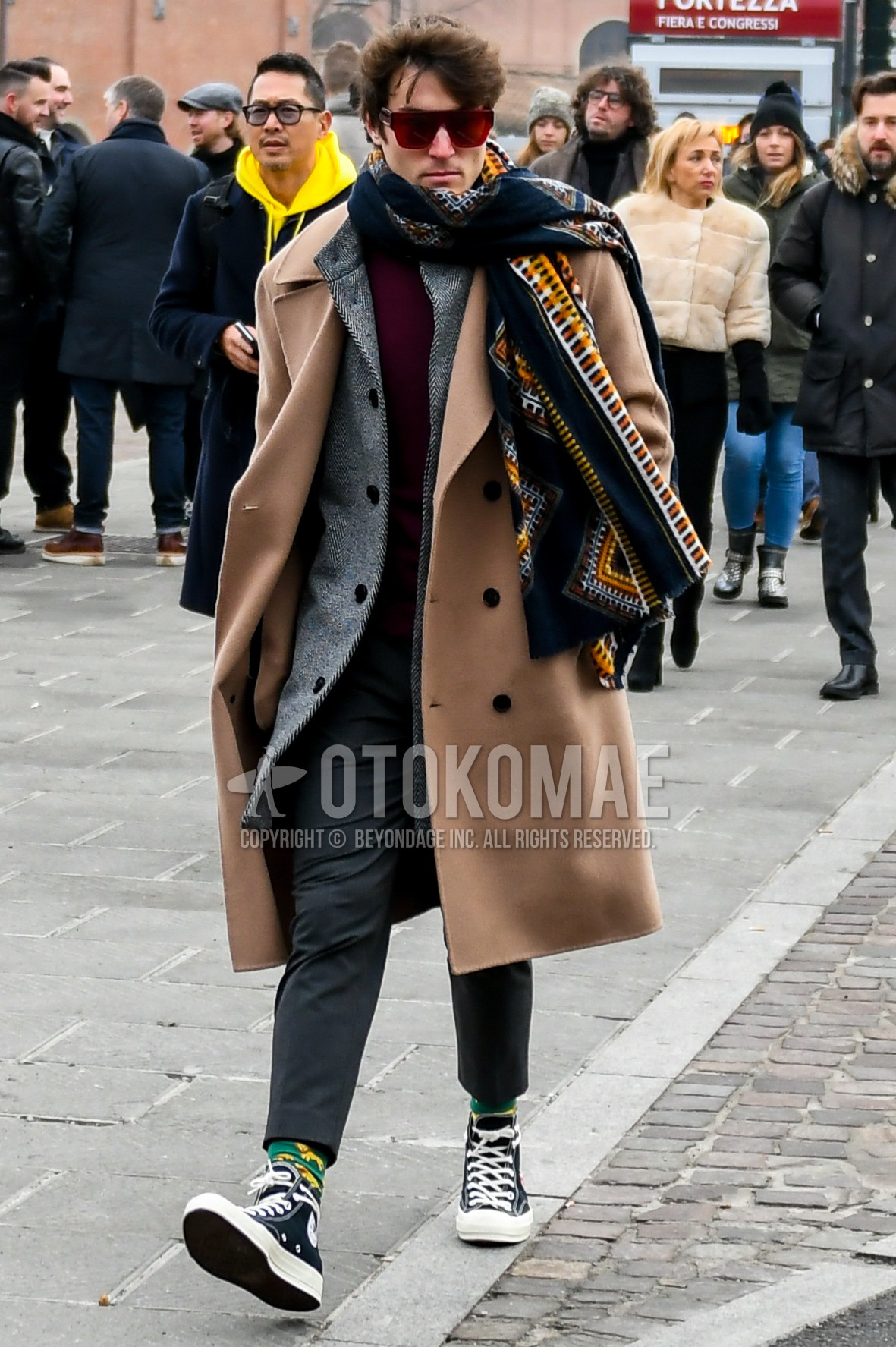 Men's winter outfit with red plain sunglasses, multi-color scarf scarf, beige plain ulster coat, gray check stand collar coat, red plain sweater, gray plain slacks, gray plain cropped pants, yellow green socks socks, black high-cut sneakers.