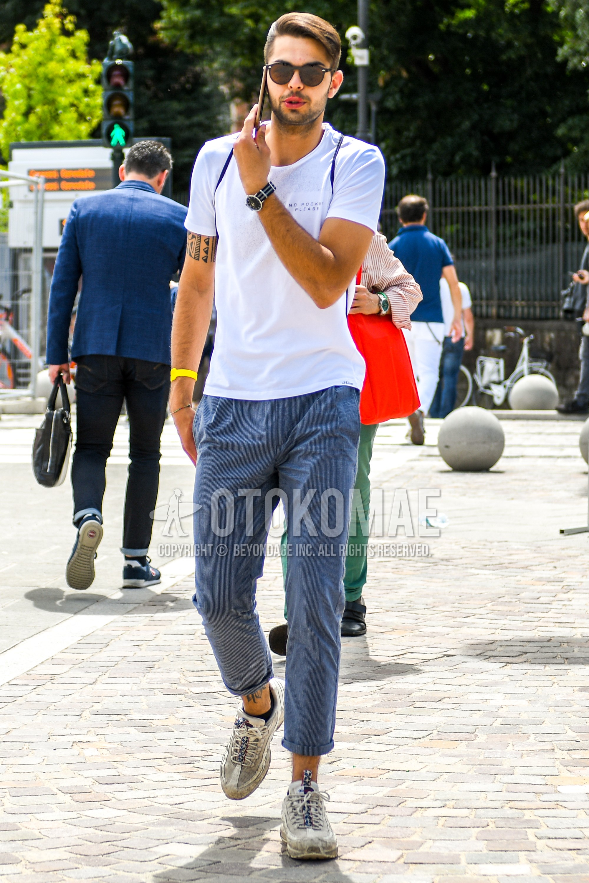 Men's summer outfit with brown plain sunglasses, white graphic t-shirt, gray stripes cotton pants, white low-cut sneakers.